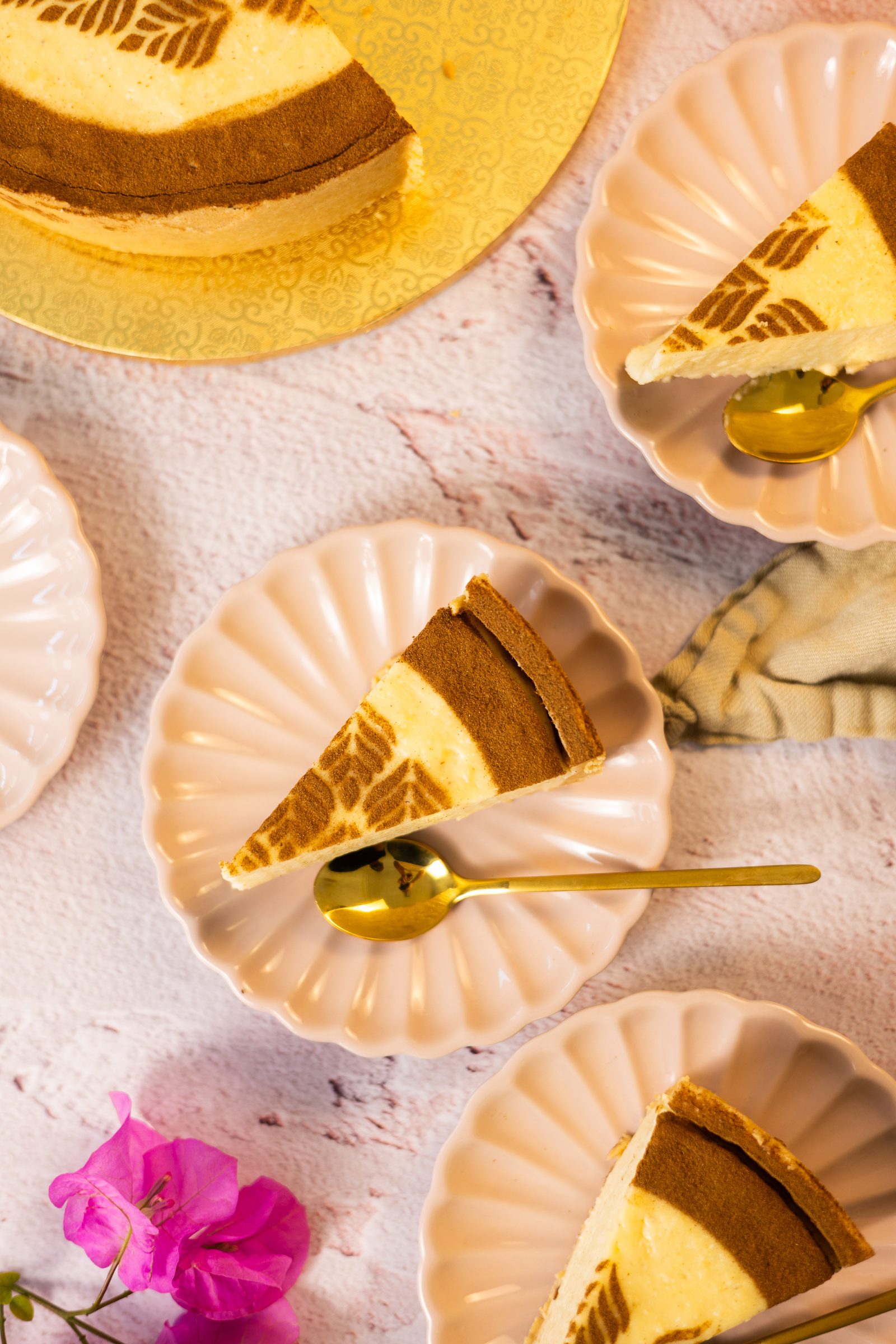 Plated slices of no bake milk tart from above with gold spoons, the cut tart and a pink flower
