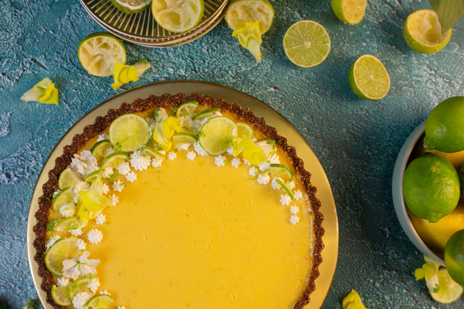 A key lime pie with a ginger and coconut crust, decorated with lime slices and flowers, from above