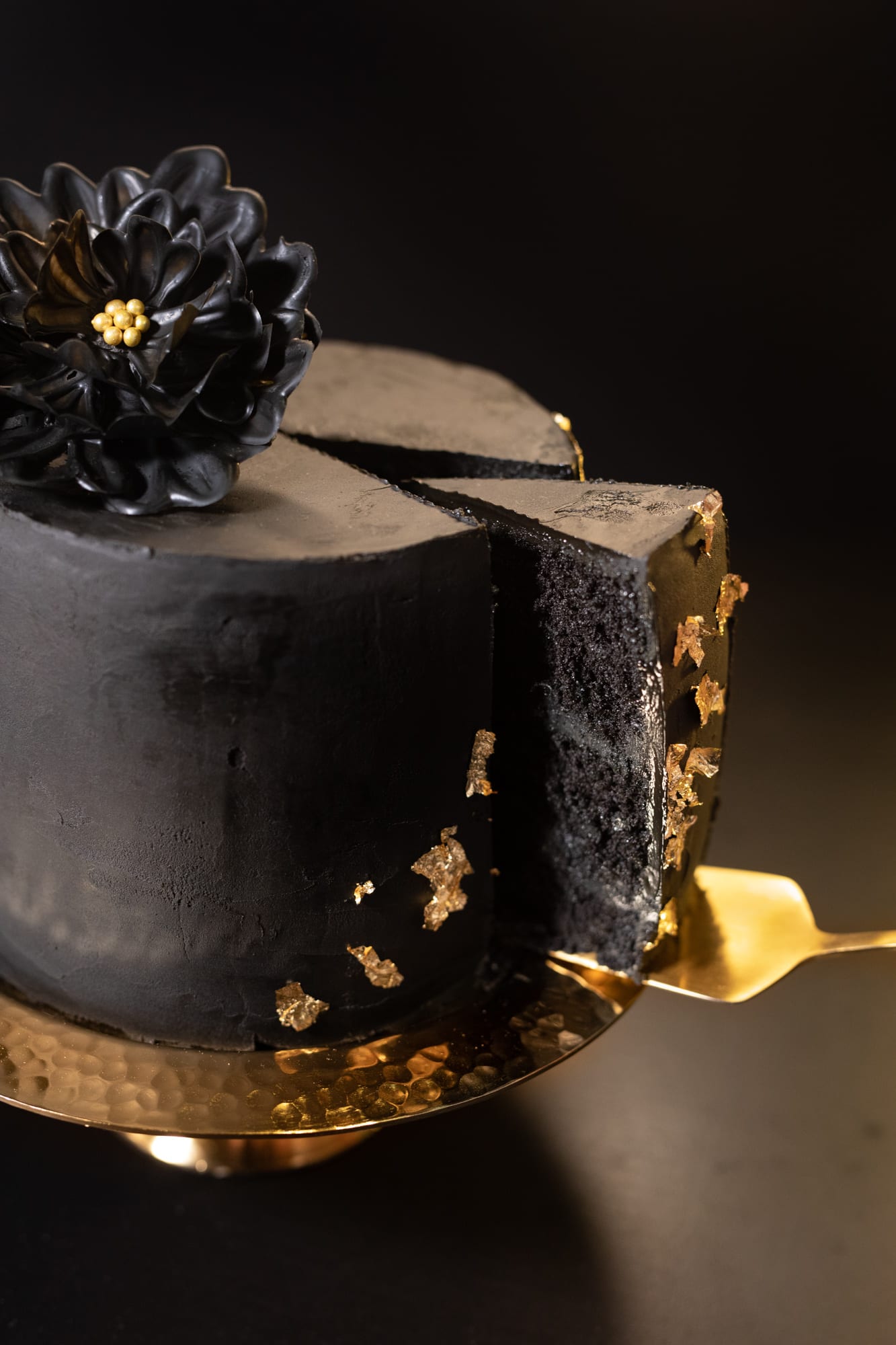A slice of black velvet cake pulled out on a gold server, showing the dark crumb