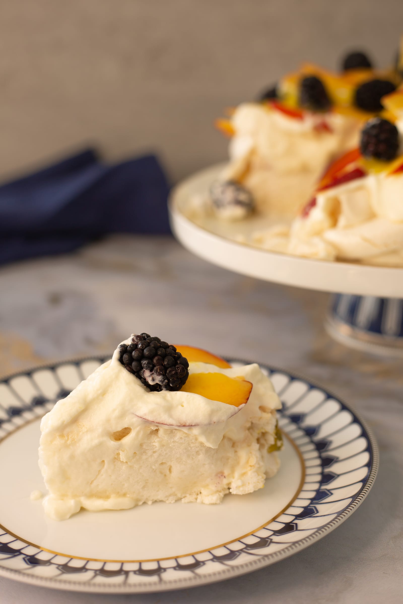 A slice of blackberry and nectarine pavlova on a blue-rimmed plate, topped with a blackberry