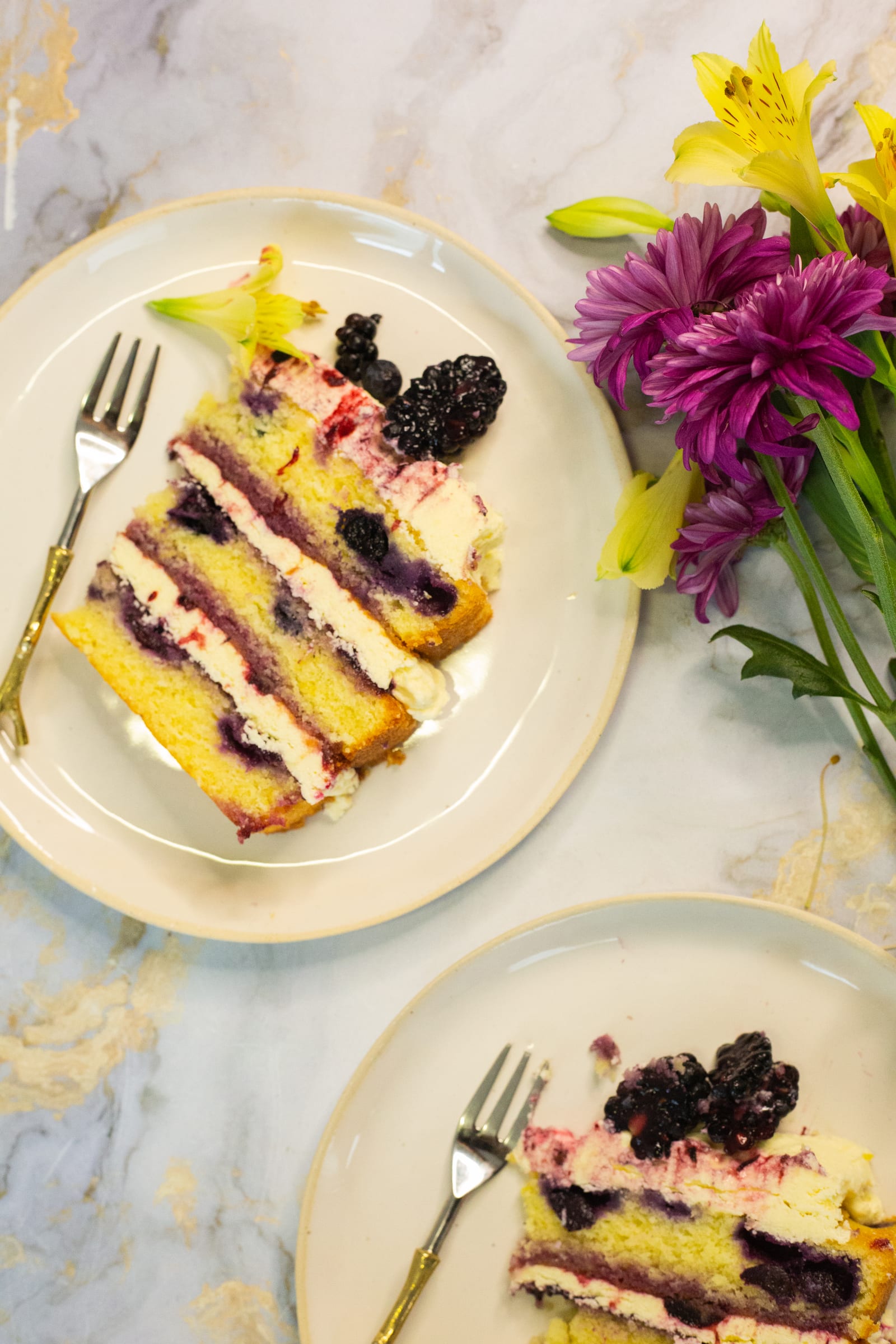 Two slices of lemon and blueberry cake on plates from above, with flowers