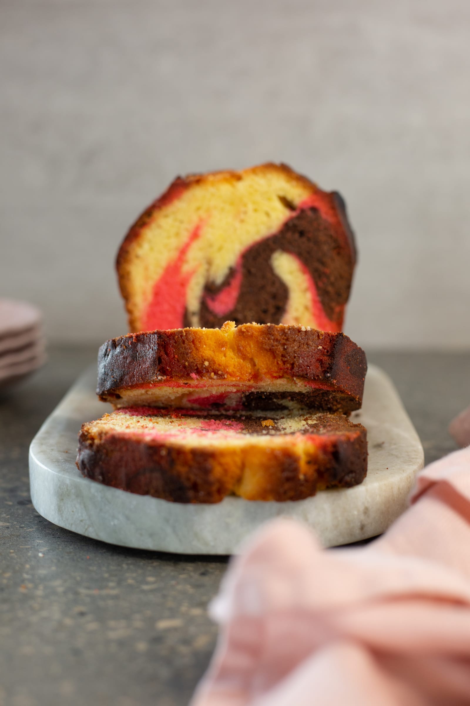 The cut end of a Neapolitan pound cake with slices laid out in front on a marble board