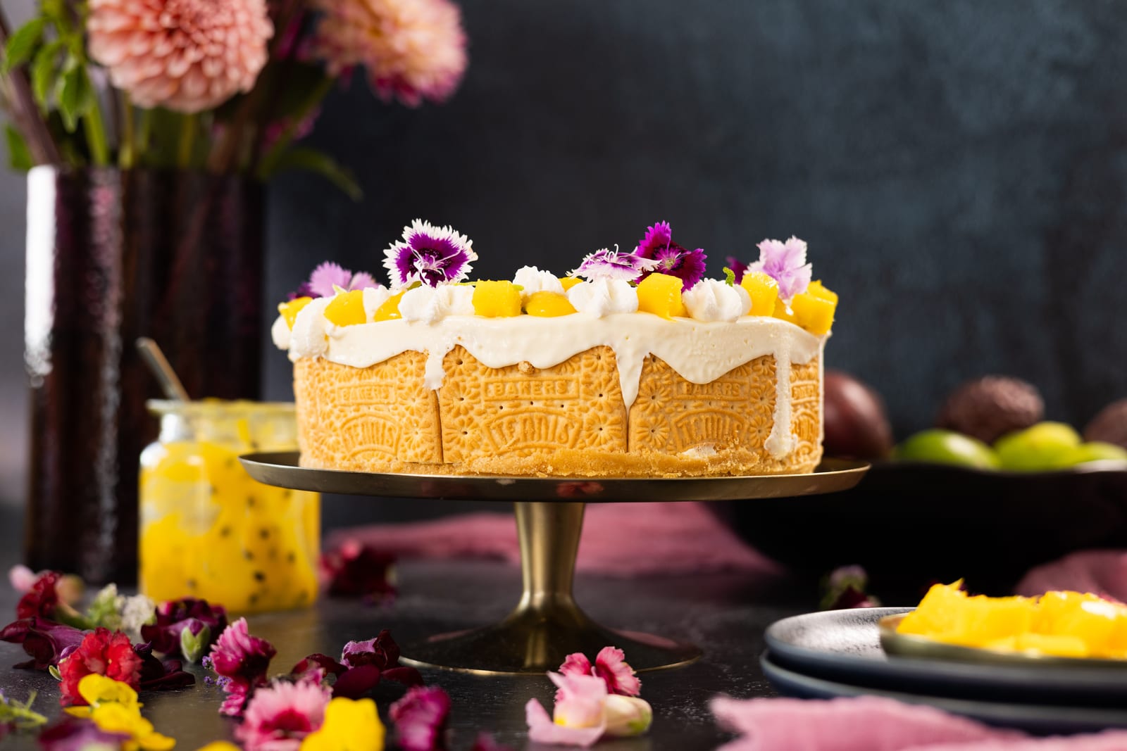 A passionfruit cheesecake ice cream cake on a gold stand, topped with edible flowers and mango