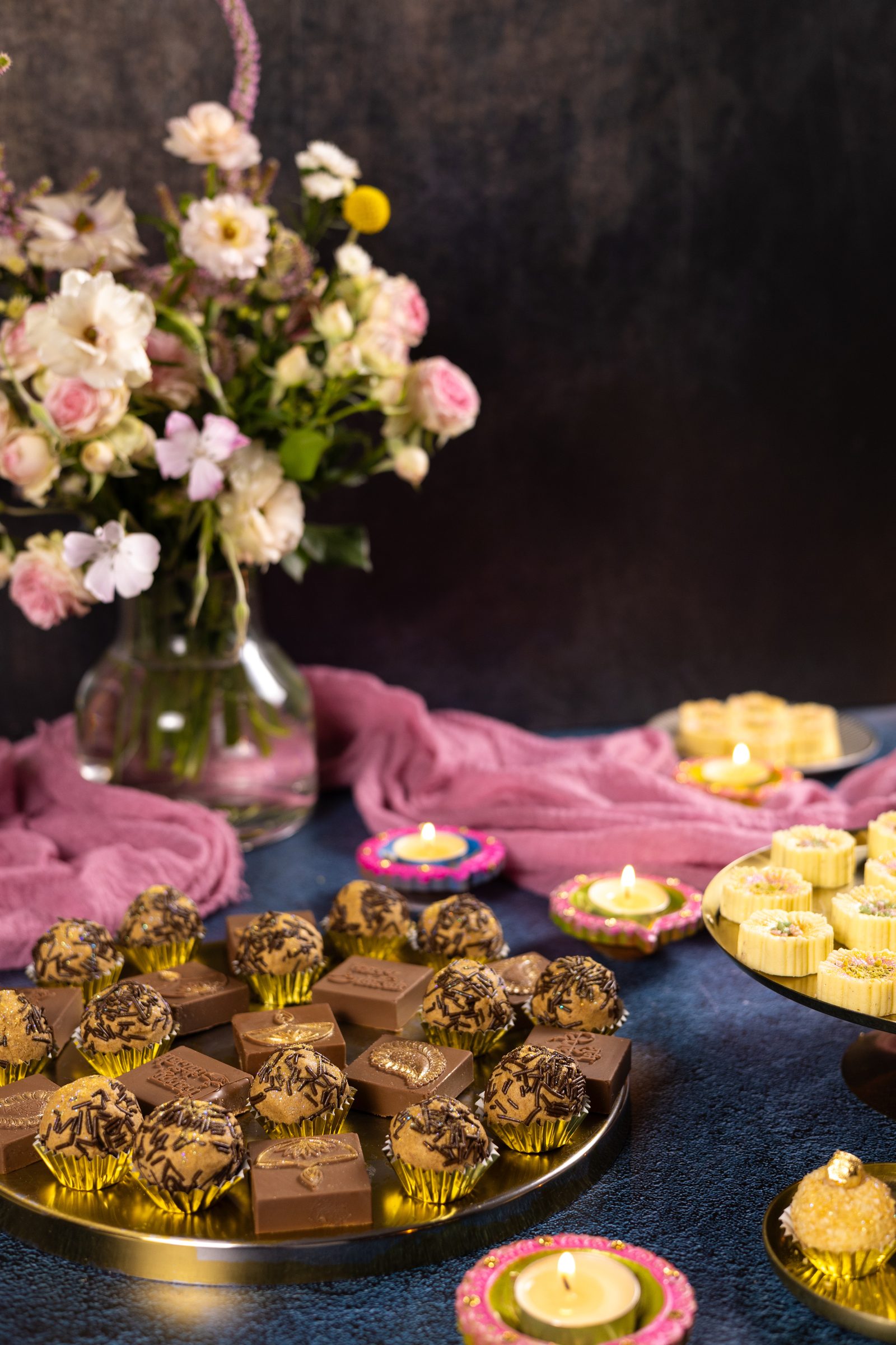 A gold platter of caramel and chocolate Simply Wonderfuls with flower-shaped Simply Wonderfuls and flowers behind, from the side
