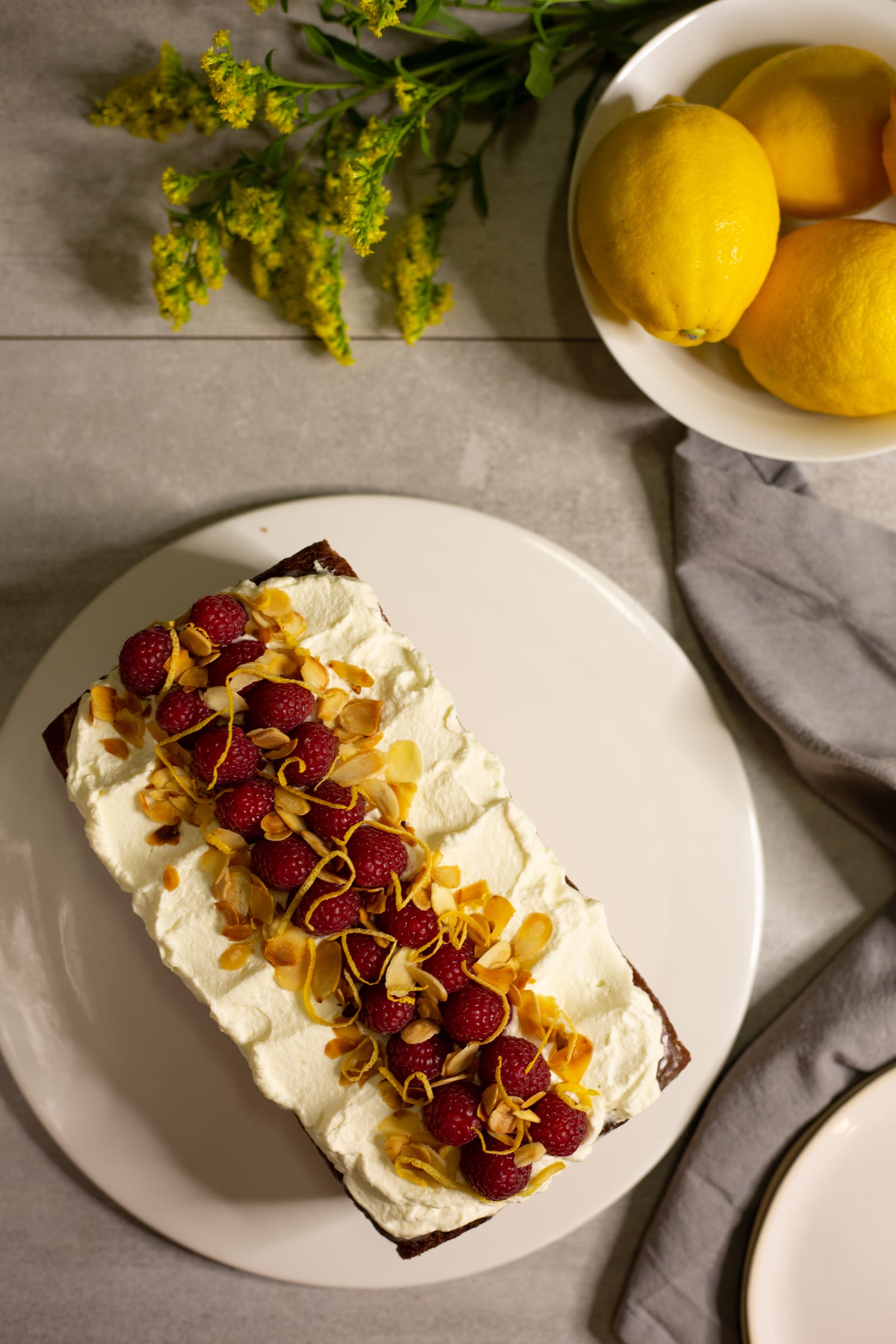 A gluten-free almond, raspberry and lemon loaf topped with cream, raspberries and flaked almonds, from above