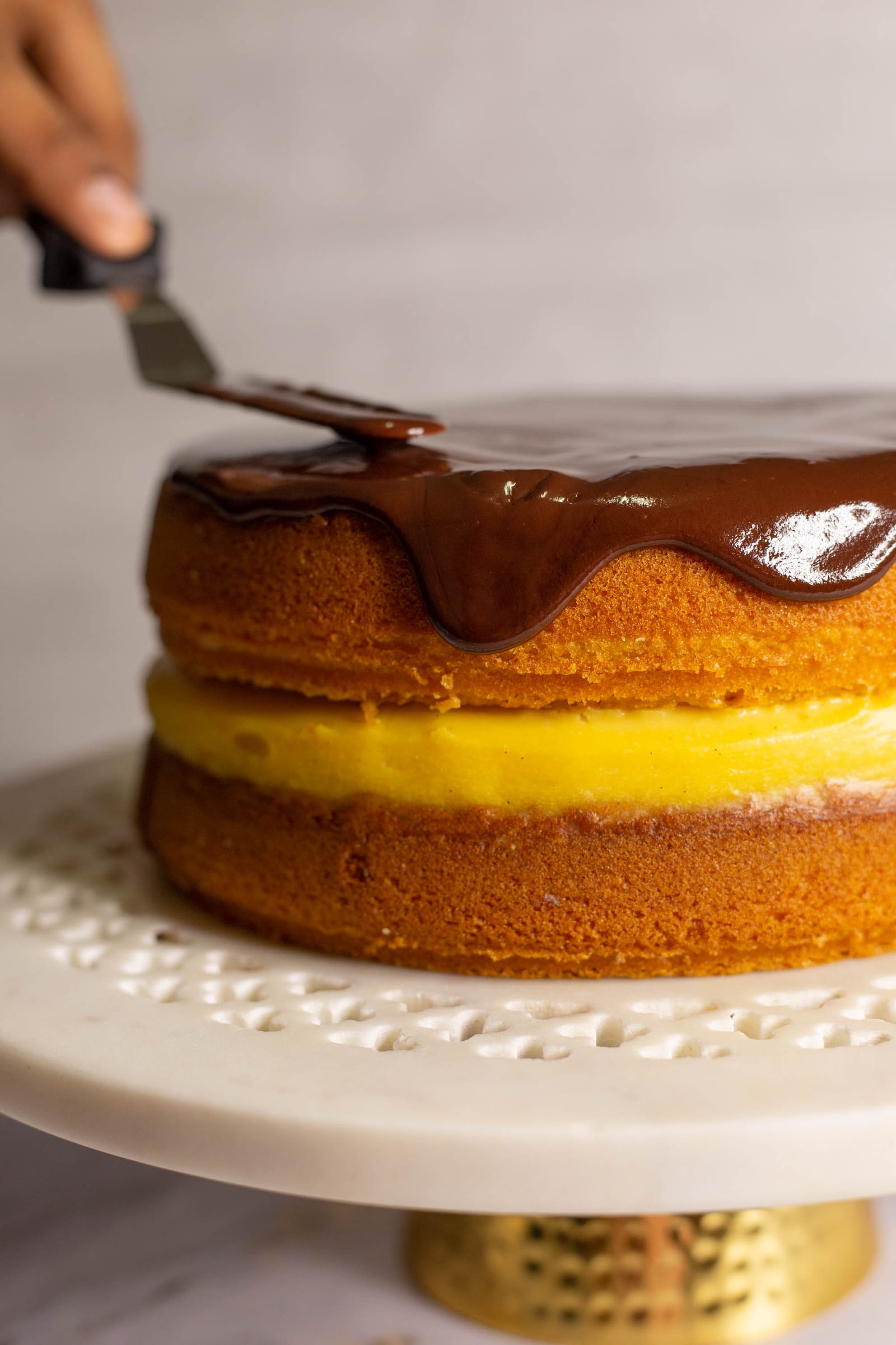 Ganache being eased over the edge of the cake with a spatula