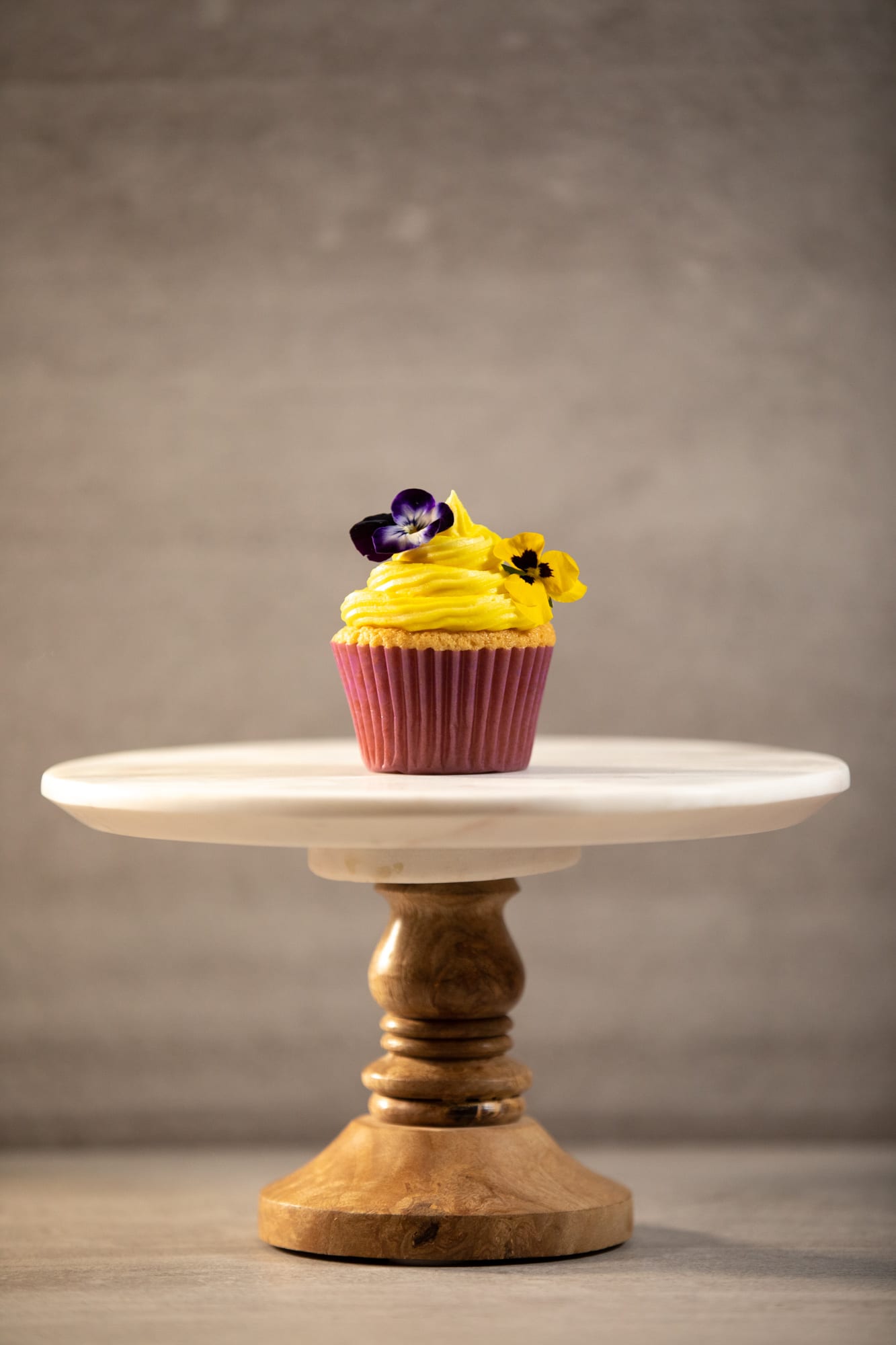 One vanilla cupcake on a white cake stand
