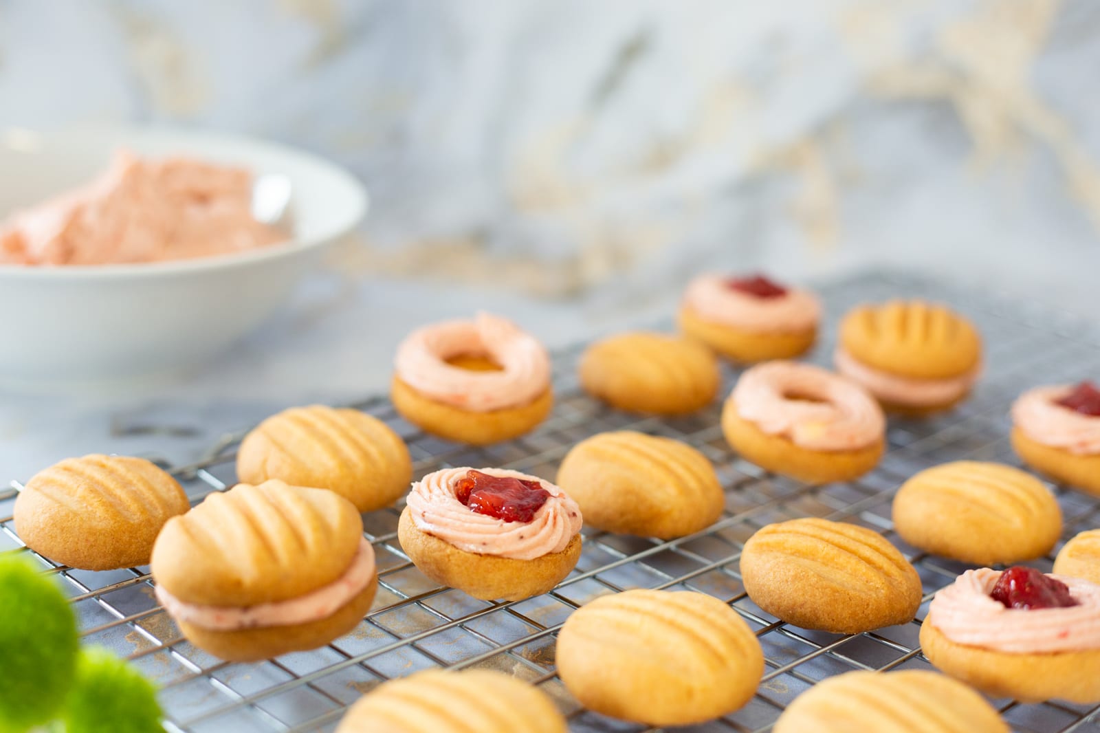 Rows of custard and jelly biscuits with jam centres, a bowl of filling behind