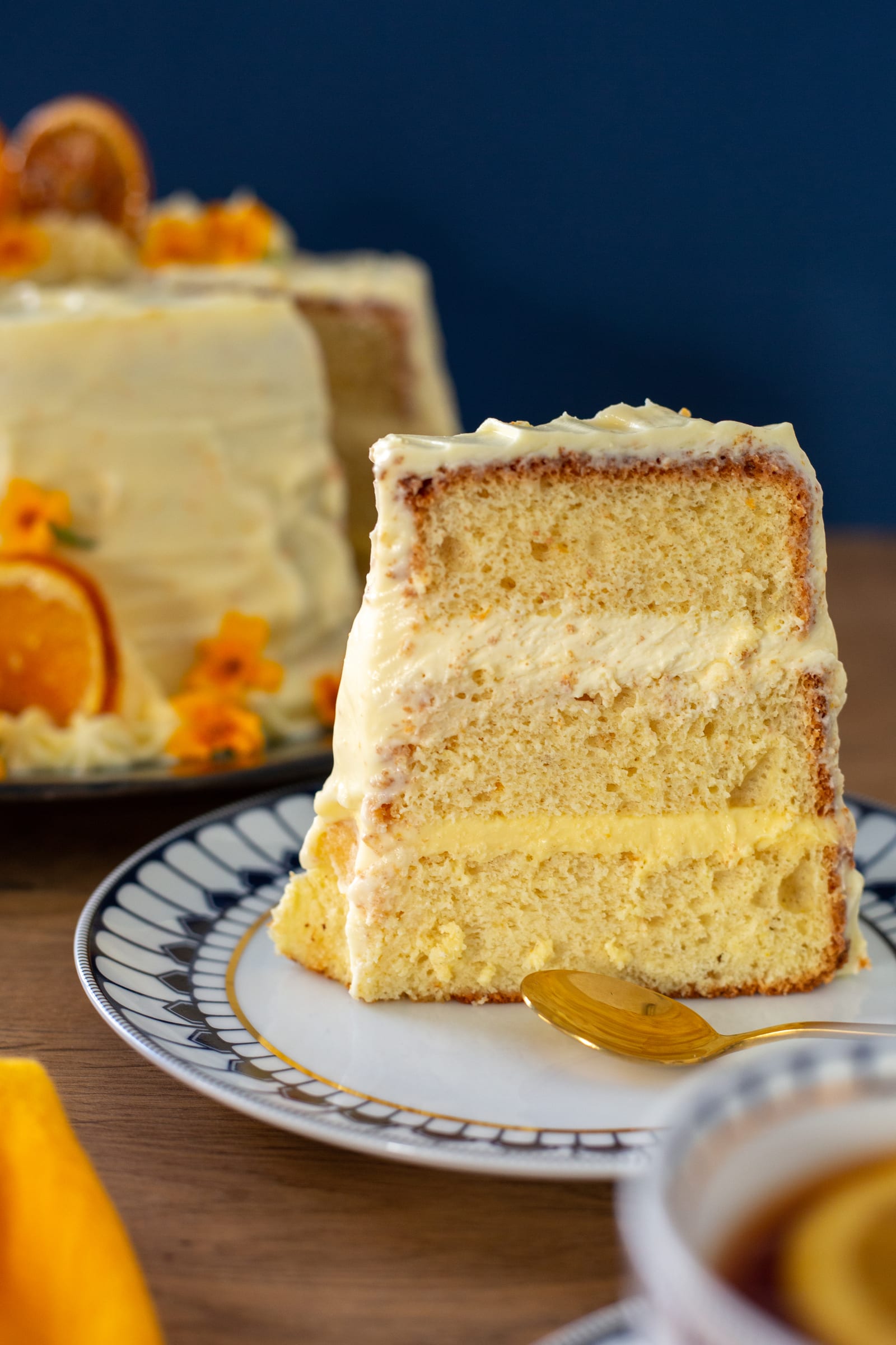 A slice of orange cream chiffon cake standing on a patterned plate, the cake behind