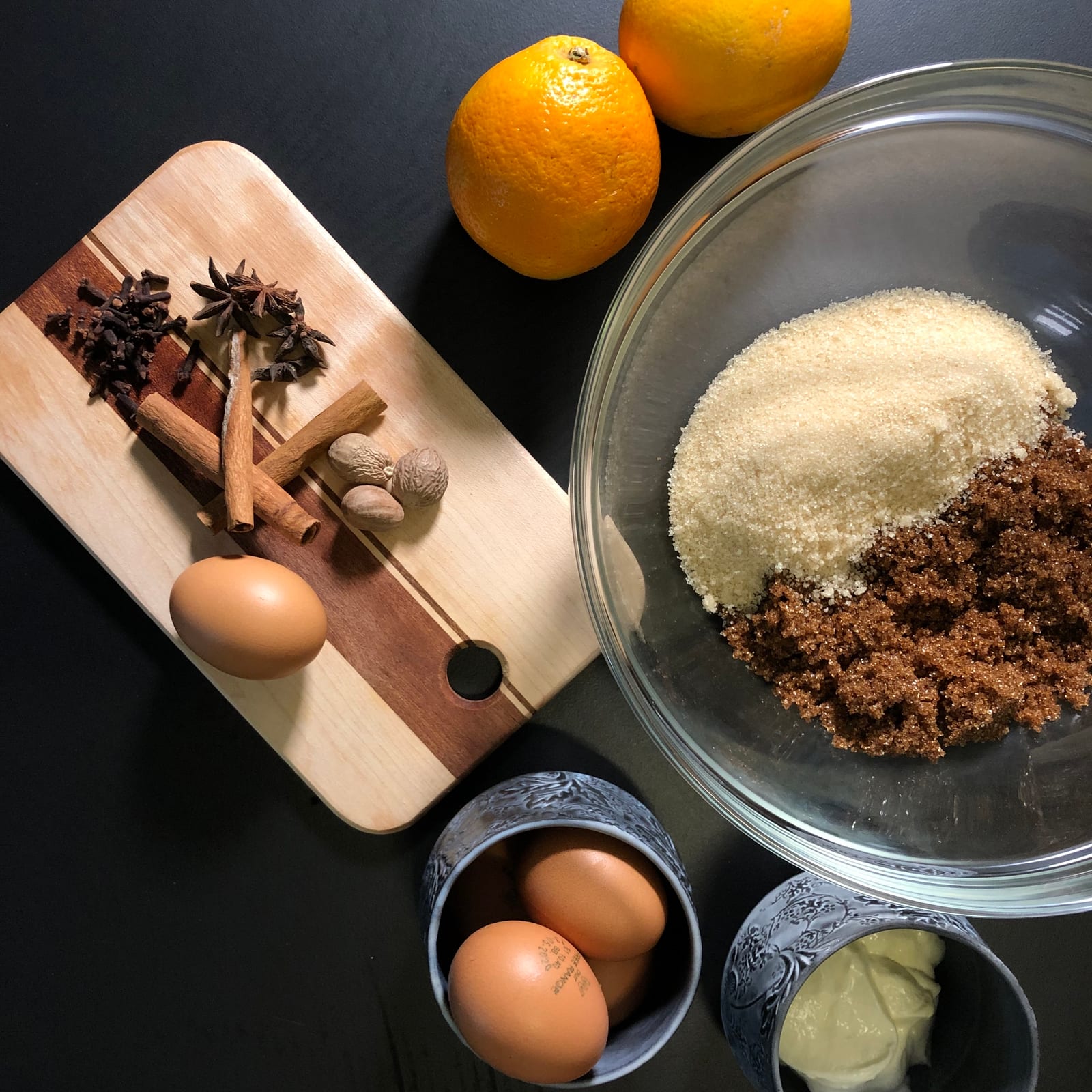 Muscovado and white sugar in a glass bowl with cinnamon, star anise, eggs and oranges