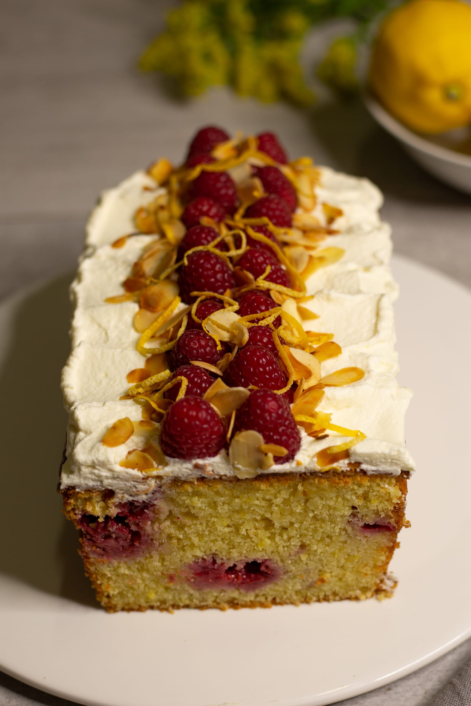 The cut end of a gluten-free almond, raspberry and lemon loaf, showing raspberries in the crumb