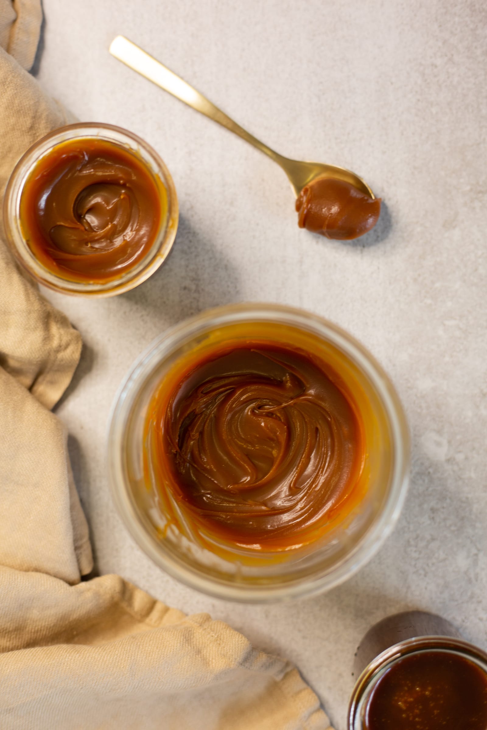 Bowls of glossy salted caramel sauce from above, with a caramel-coated gold spoon