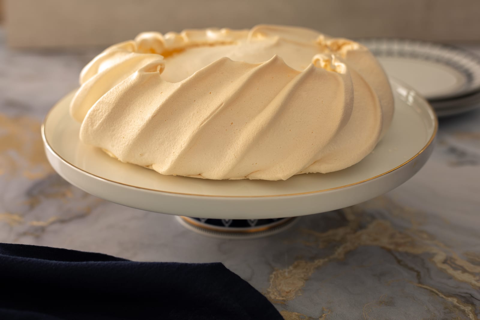 The baked meringue shell on a cake stand, its swirled ridges crisp and pale