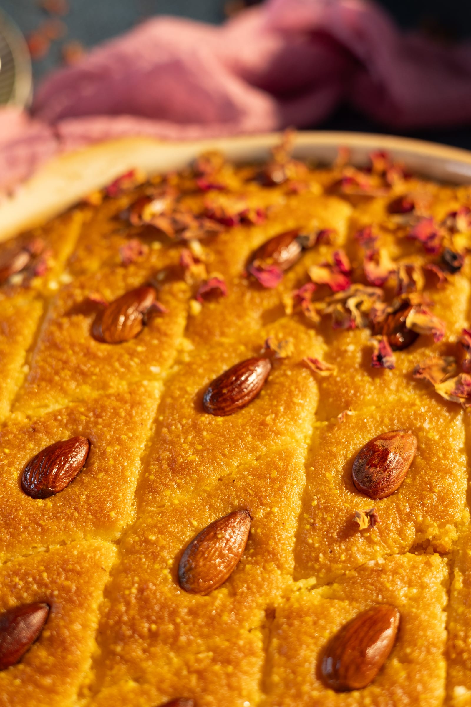 Close-up of syrup-soaked basbousa with almonds and rose petals