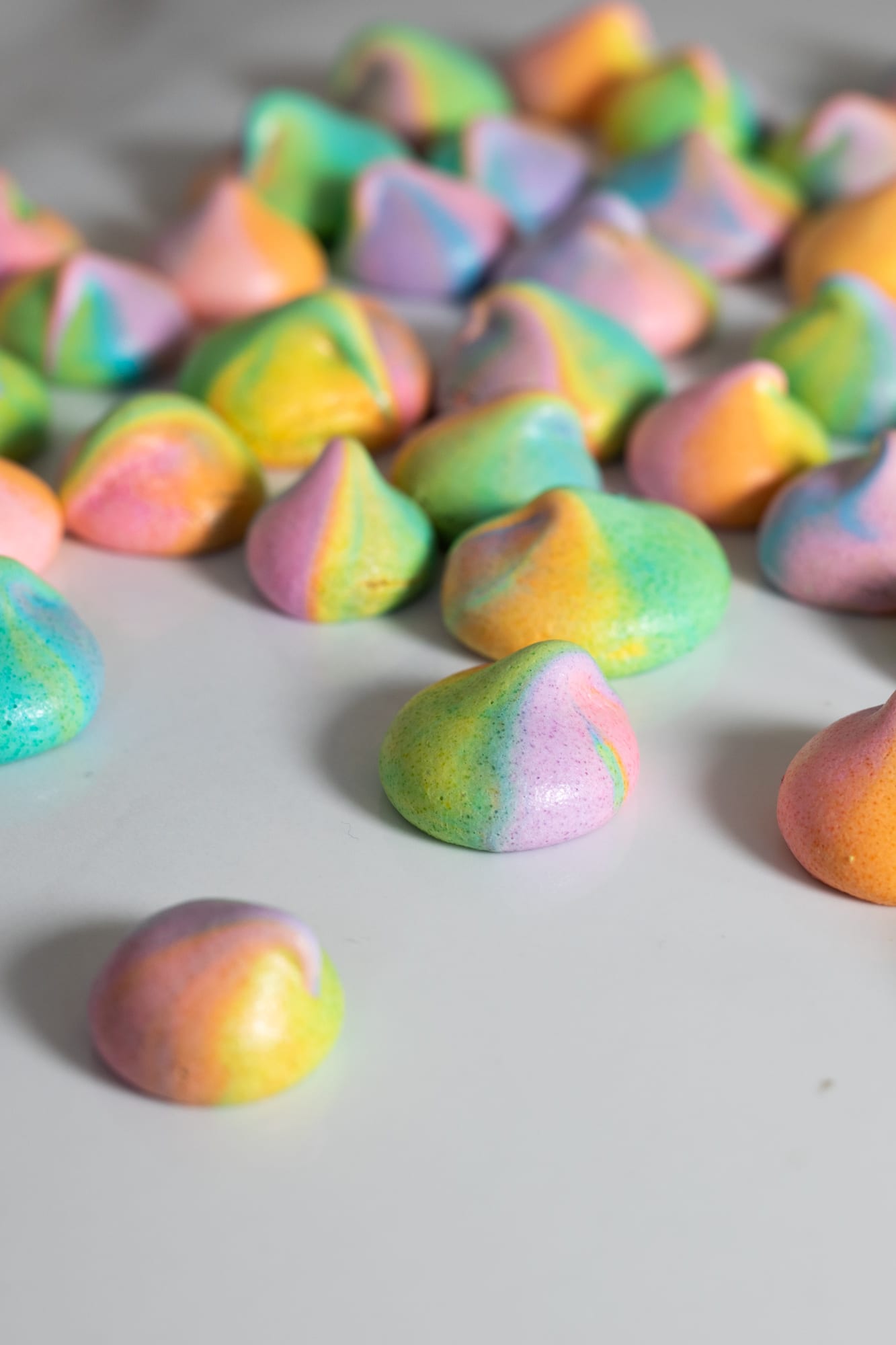 Rainbow meringue kisses on a white surface, one in focus in front