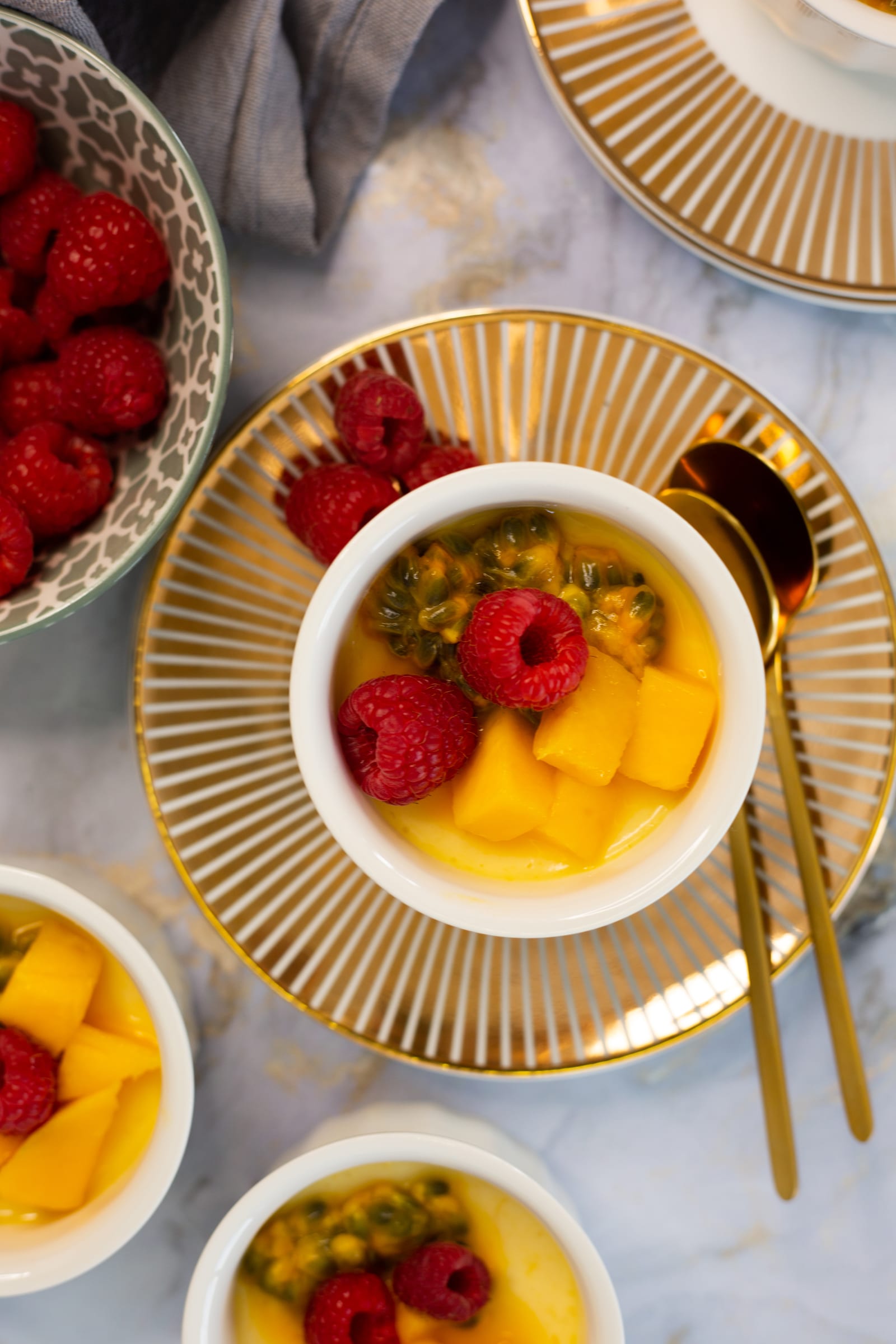 A coconut, mango and granadilla baked yogurt close up from above, with a bowl of raspberries