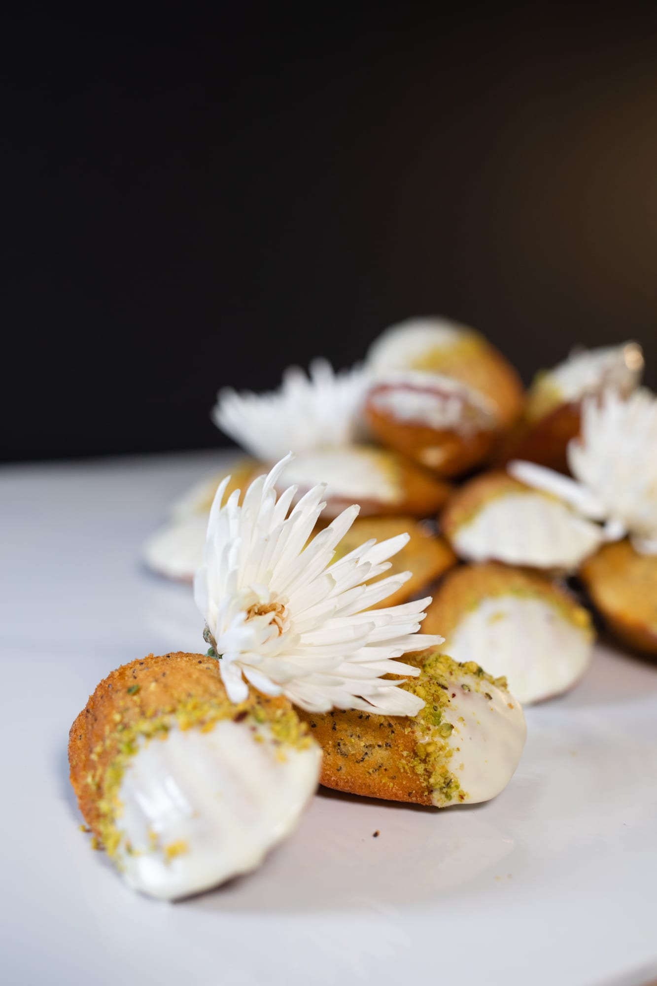 A lemon and poppyseed madeleine with a flower in front of the pile, against a black background