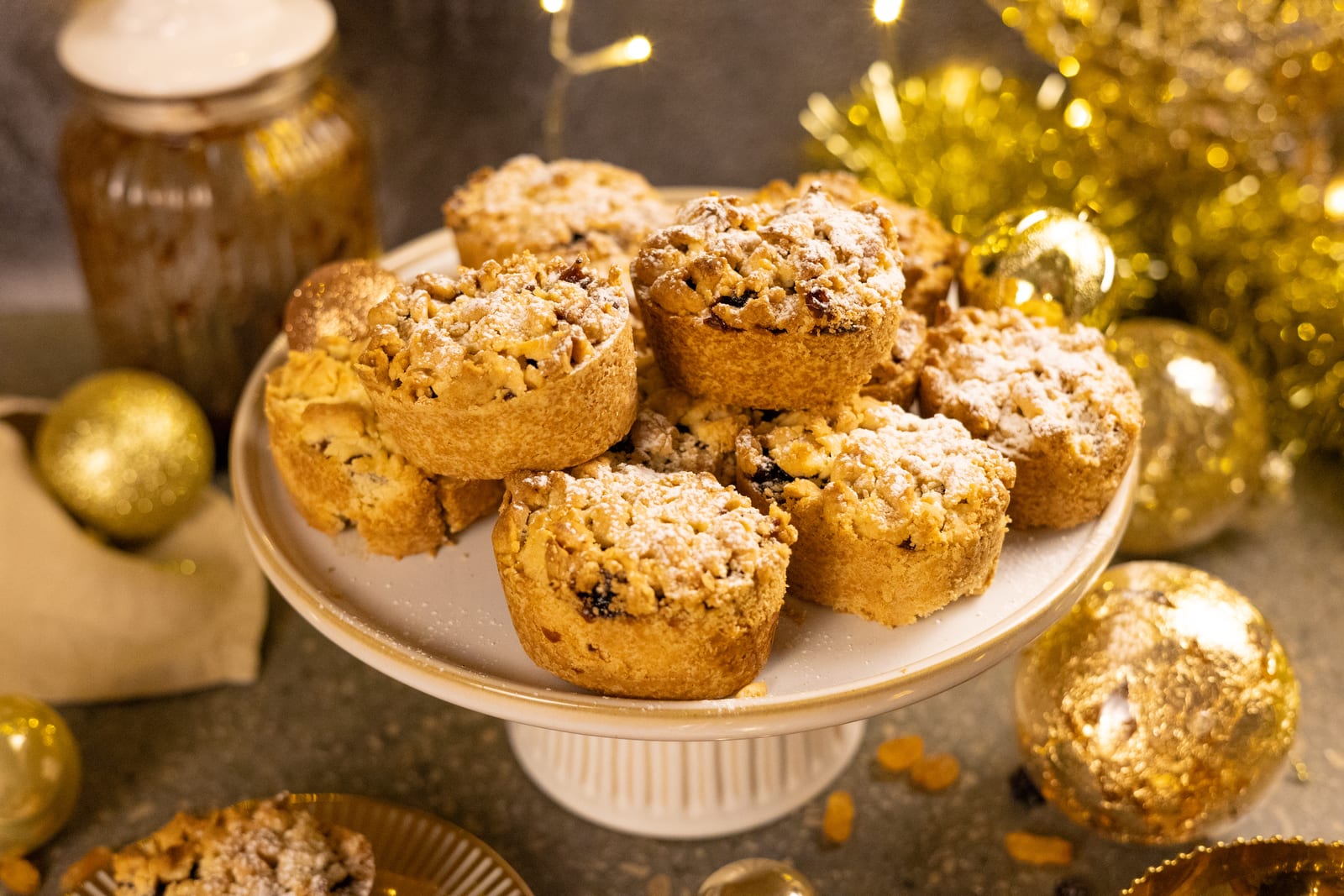 Fruit mince pies dusted with icing sugar on a cake stand, with gold Christmas decorations