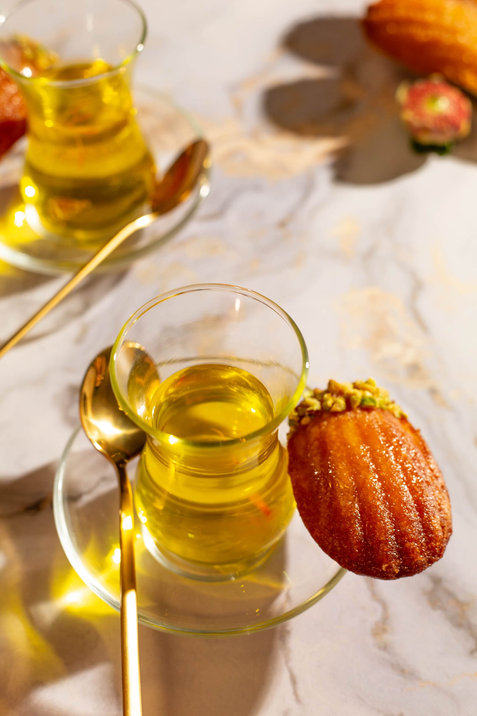 A madeleine dipped in pistachio leaning on the saucer of a tea glass