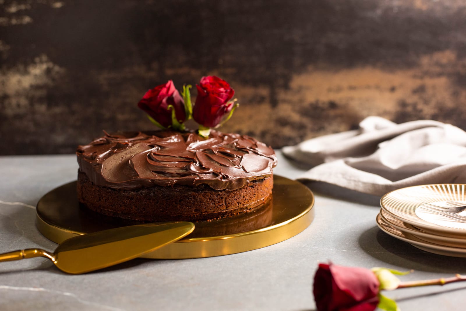A whole chocolate and beetroot cake on a gold board against dark wood, plates beside it