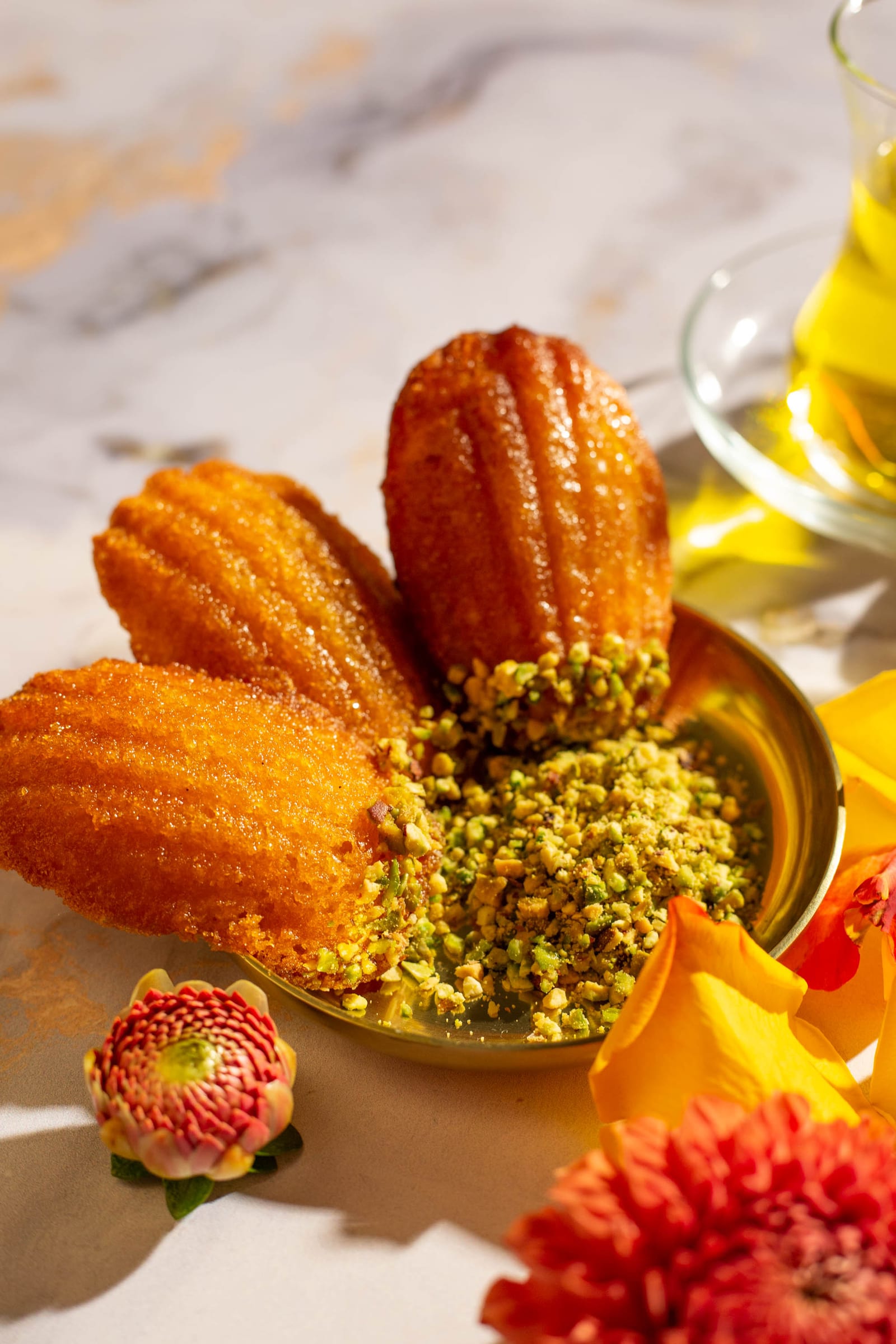 Glazed orange blossom water madeleines around a pile of crushed pistachios in a gold dish