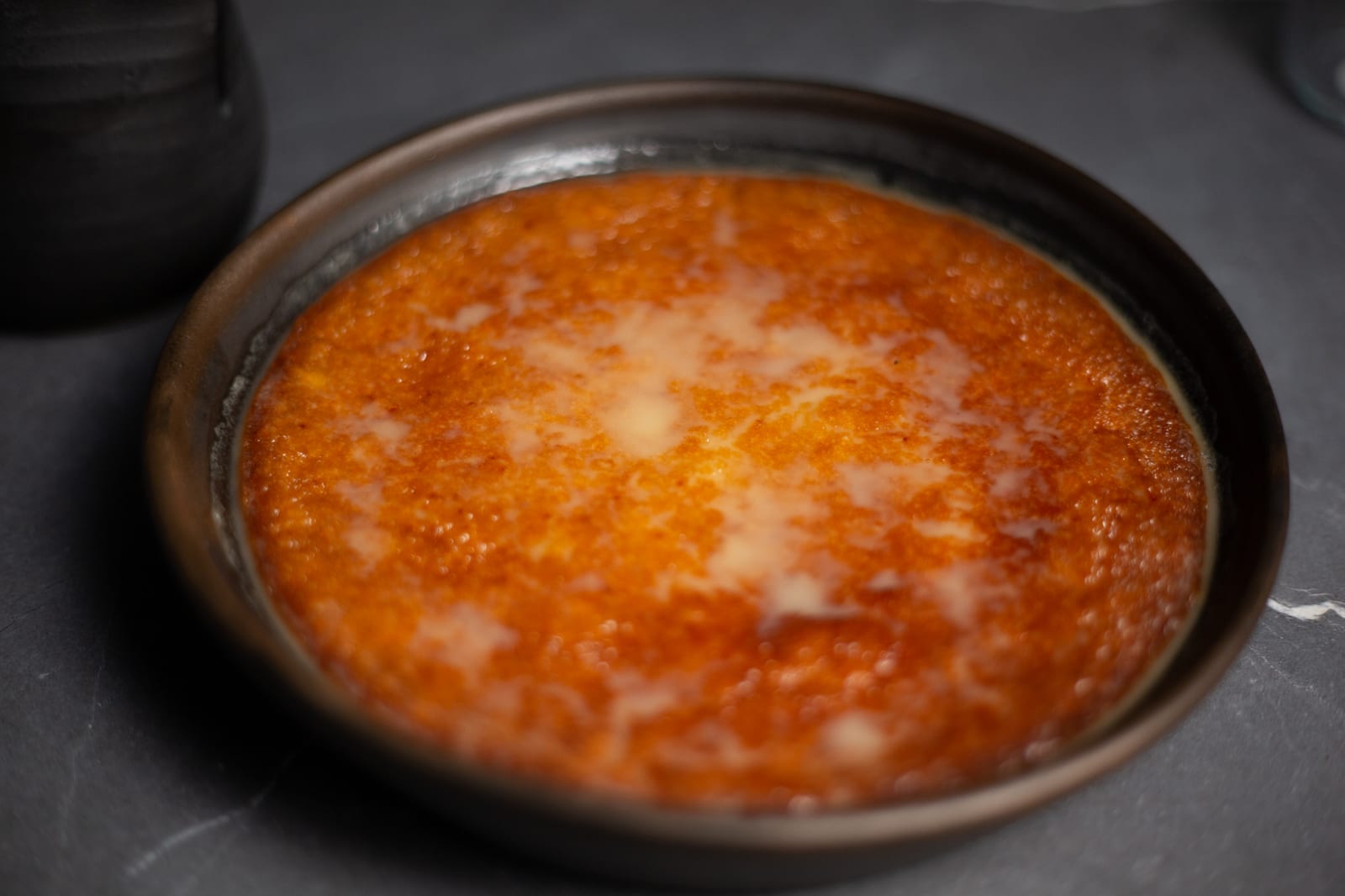 A caramelised malva pudding soaked in sauce, in a dark dish
