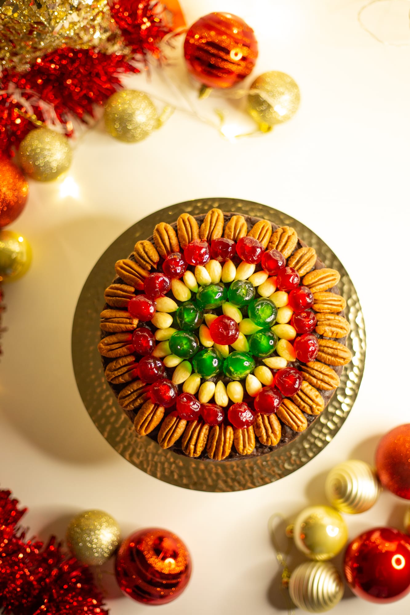 A boozy fruit cake on a gold cake stand with baubles and tinsel, from above
