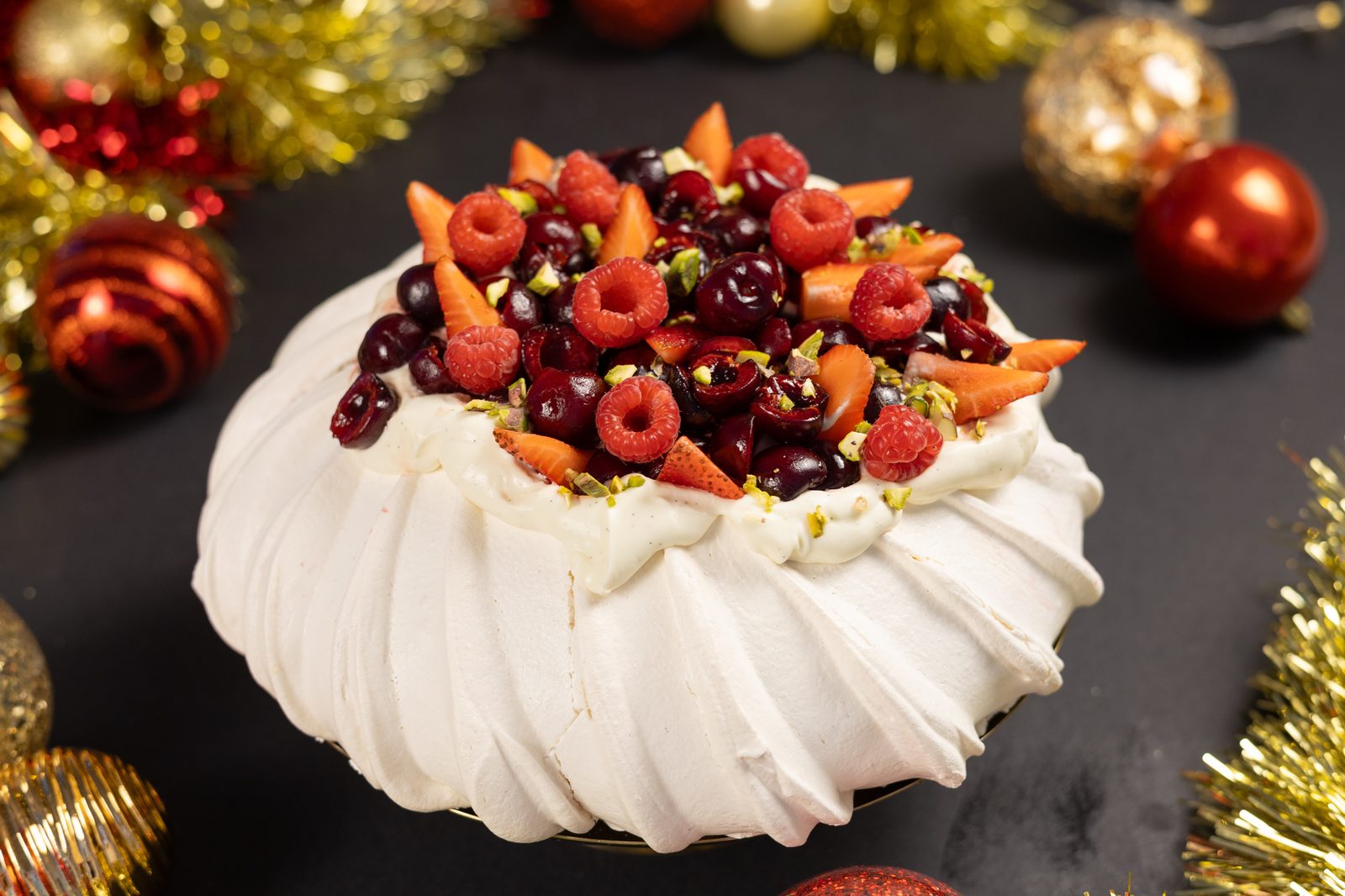 A very berry pavlova topped with cherries and raspberries among Christmas tinsel and baubles