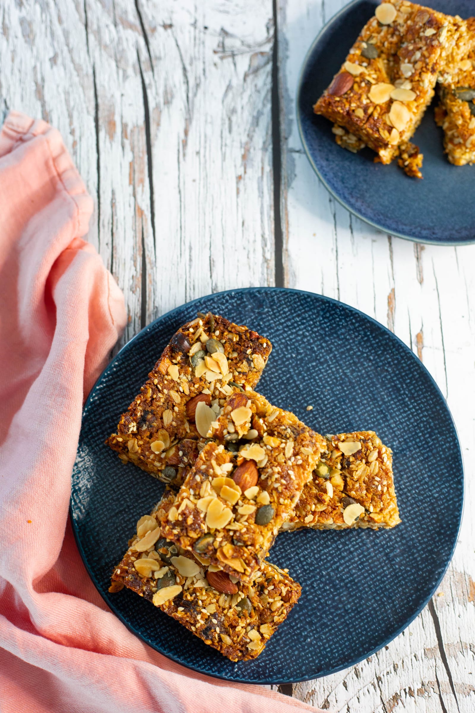 Date and nut caramel bars on a navy plate with pink linen, from above at a slight angle