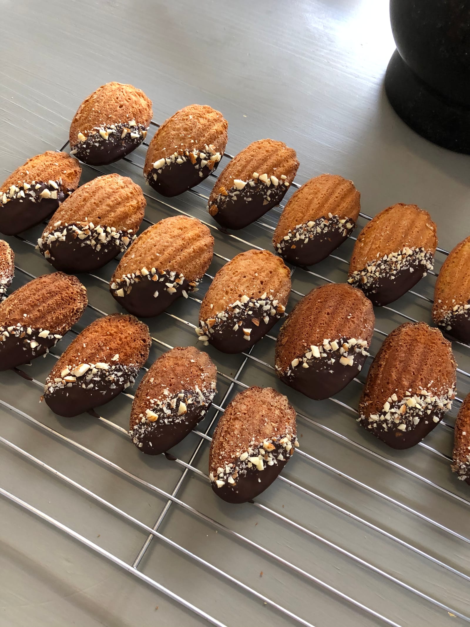 Brown butter and almond madeleines dipped in chocolate and chopped almonds on a cooling rack