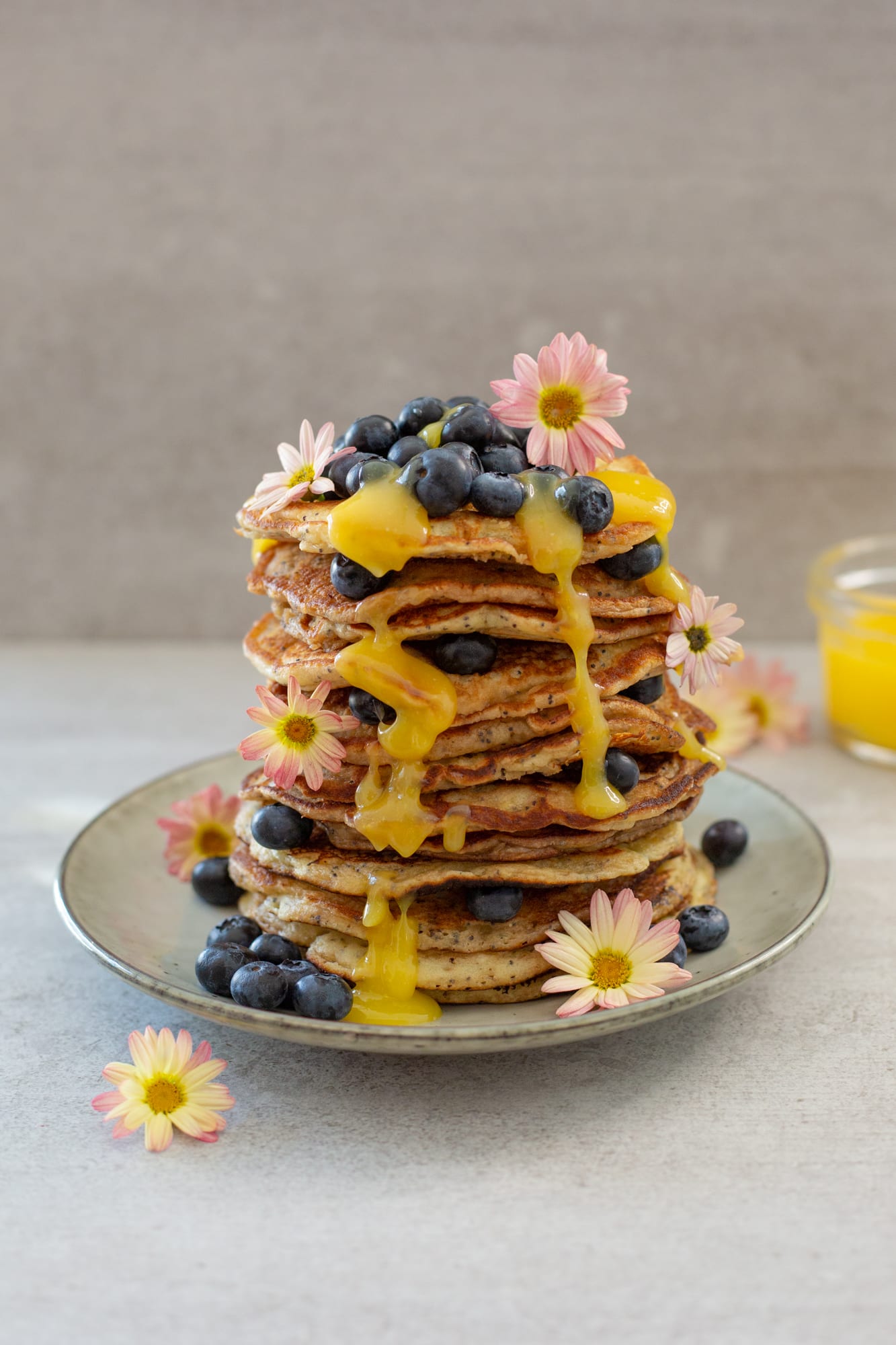 A tall stack of lemon and poppyseed pancakes dripping with lemon curd, blueberries on top