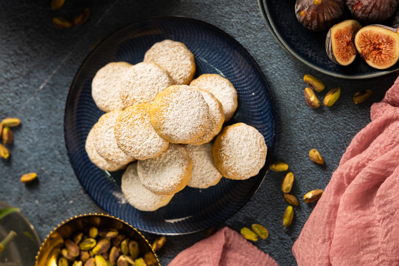 A plate of fig and pistachio ma'amoul dusted with icing sugar, from above