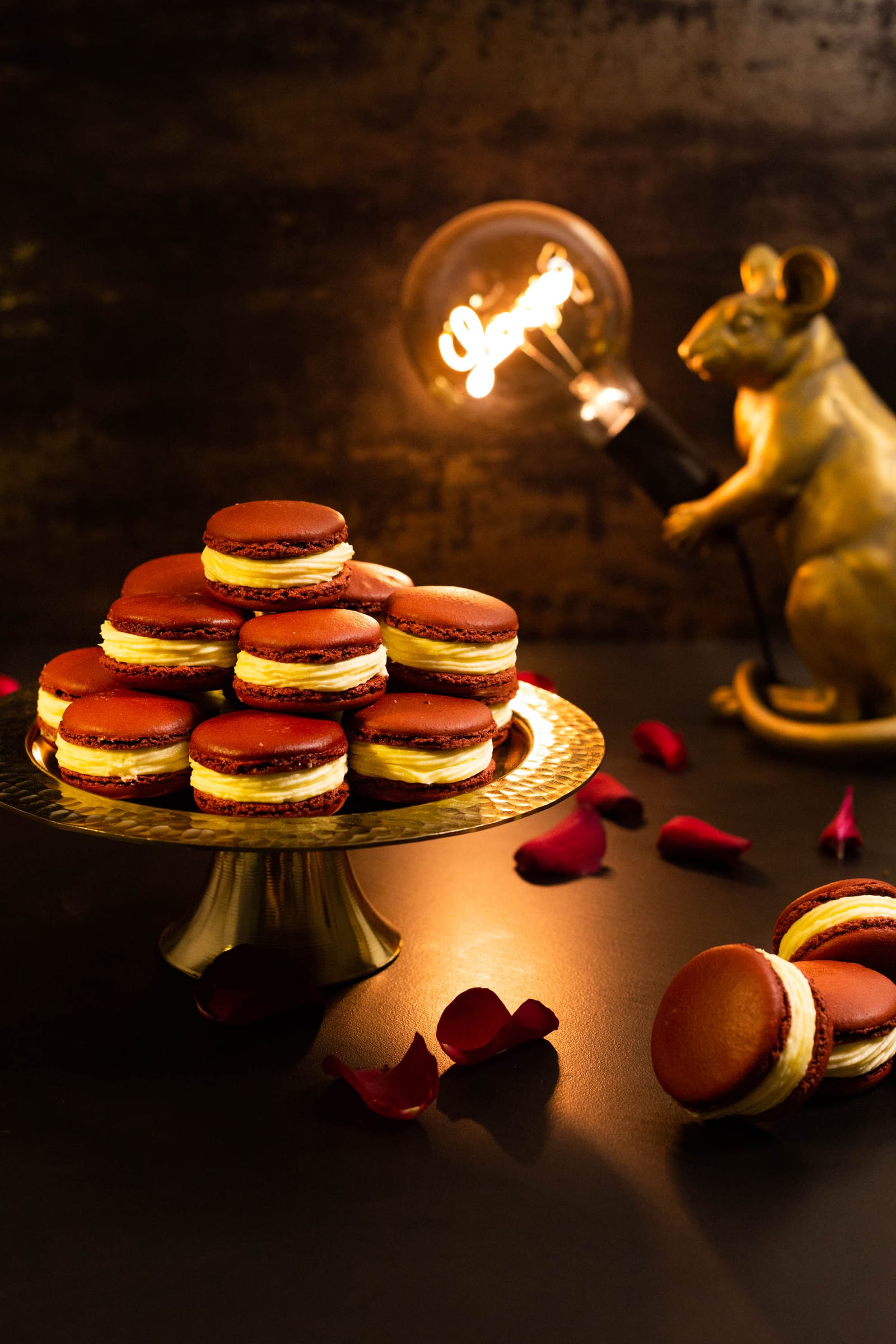 Red velvet macarons on a gold stand beside a lit gold lamp