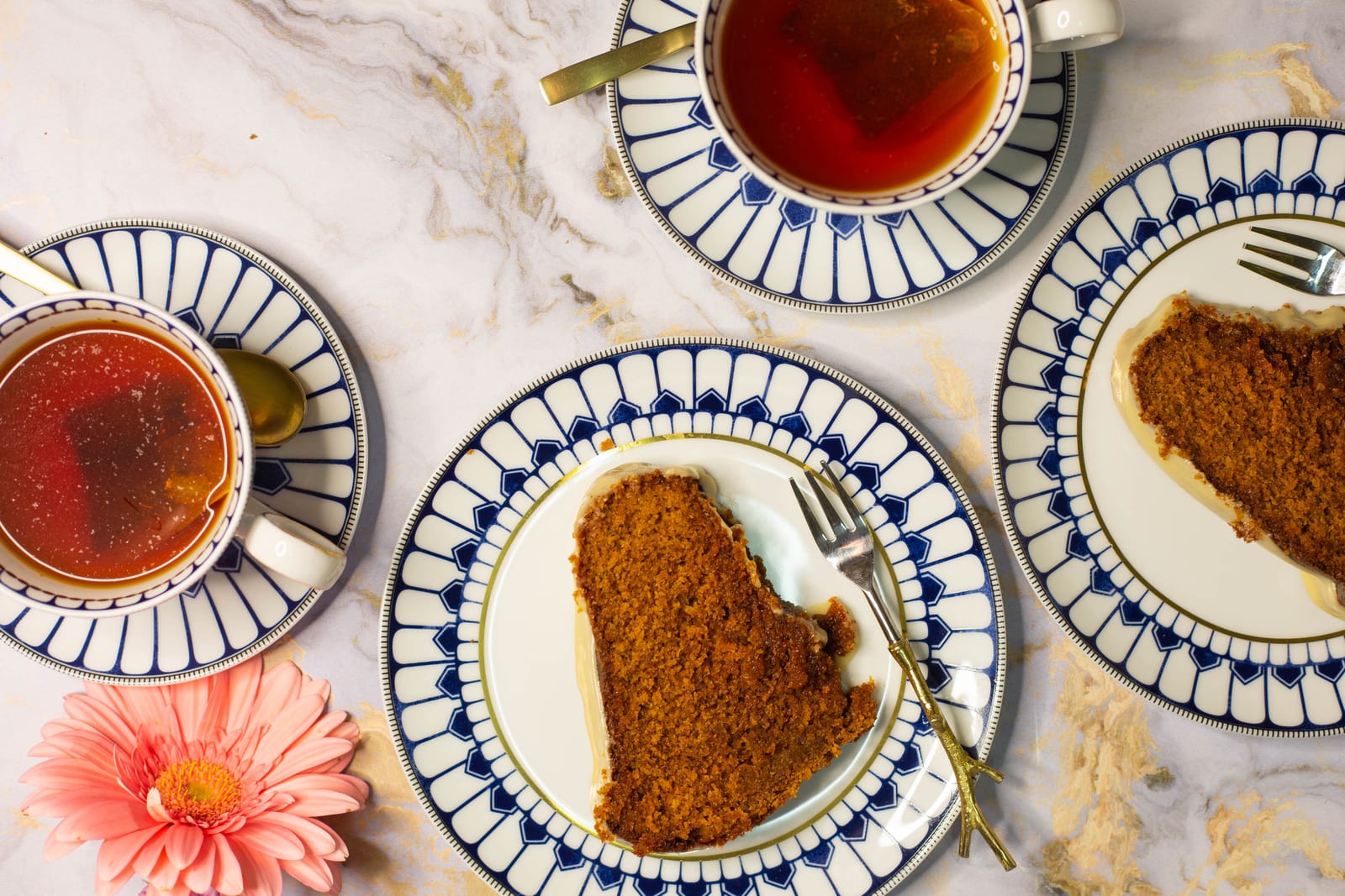 Two slices of rooibos and honey bundt on blue and white plates with cups of rooibos tea and gold forks, from above
