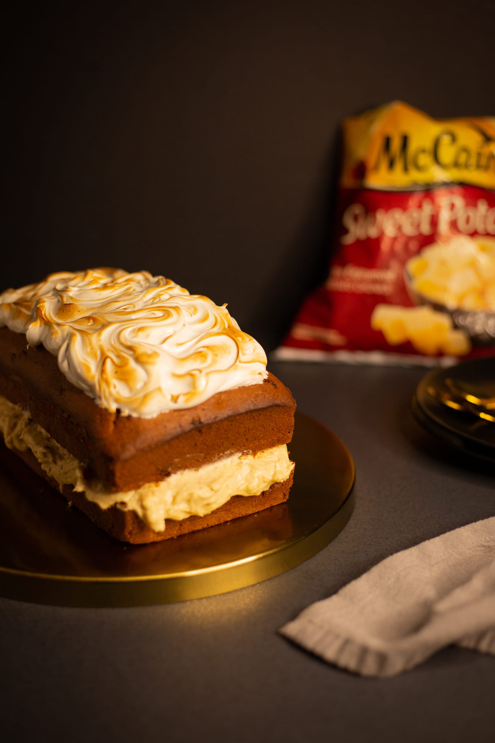 A whole sweet potato loaf with toasted meringue on top on a gold board
