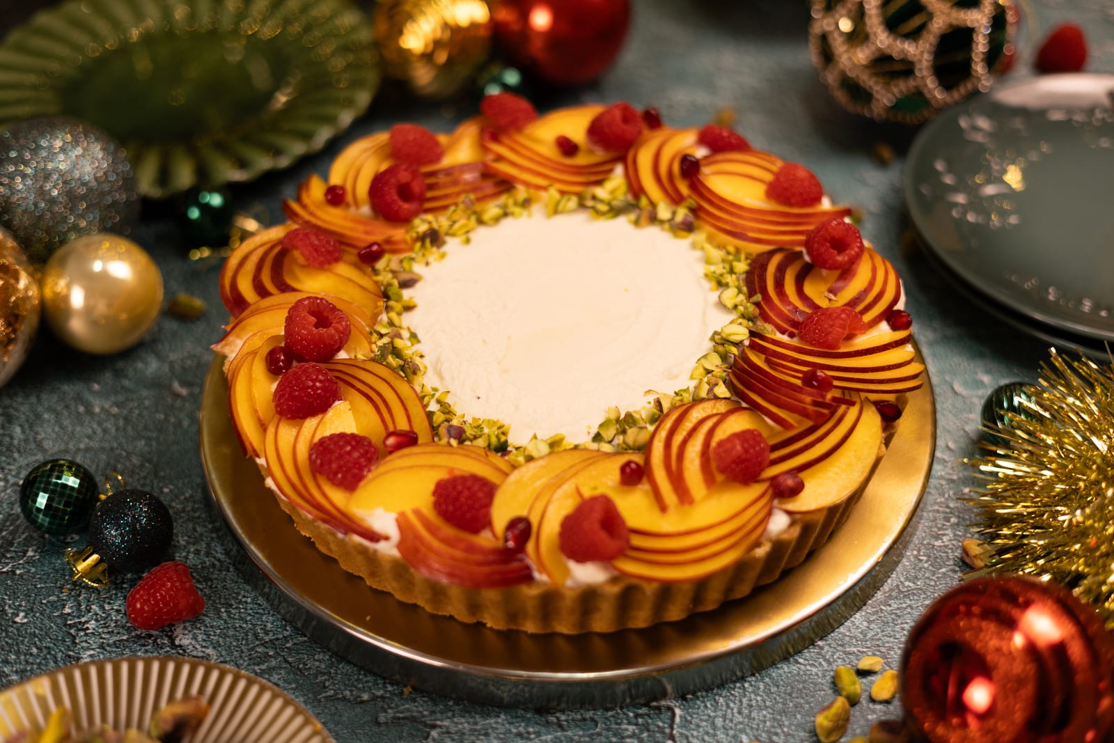 A Cremora tart topped with a ring of nectarine slices, raspberries and pistachios, among Christmas baubles