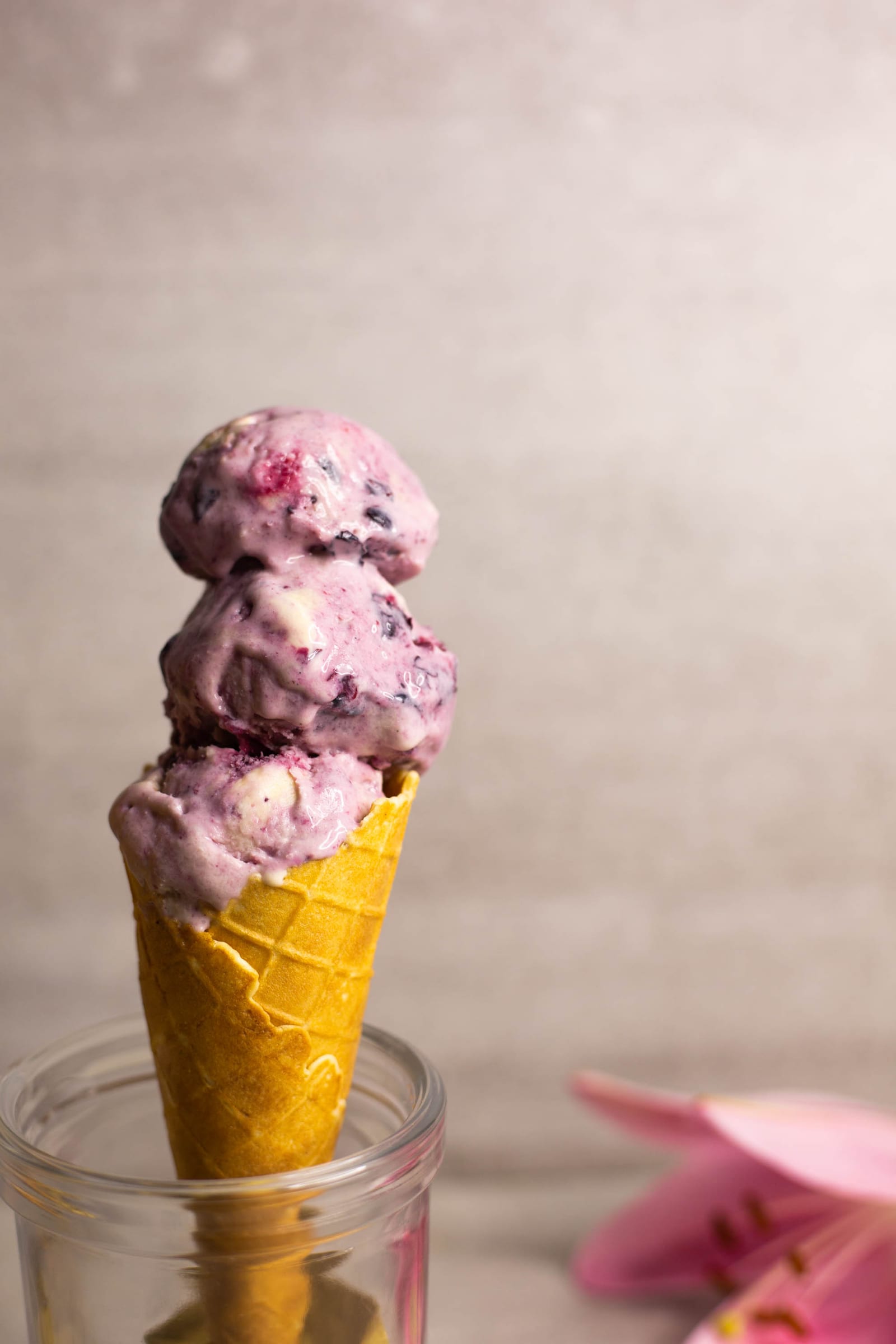 A waffle cone of blueberry swirl ice cream standing in a glass jar, from the side
