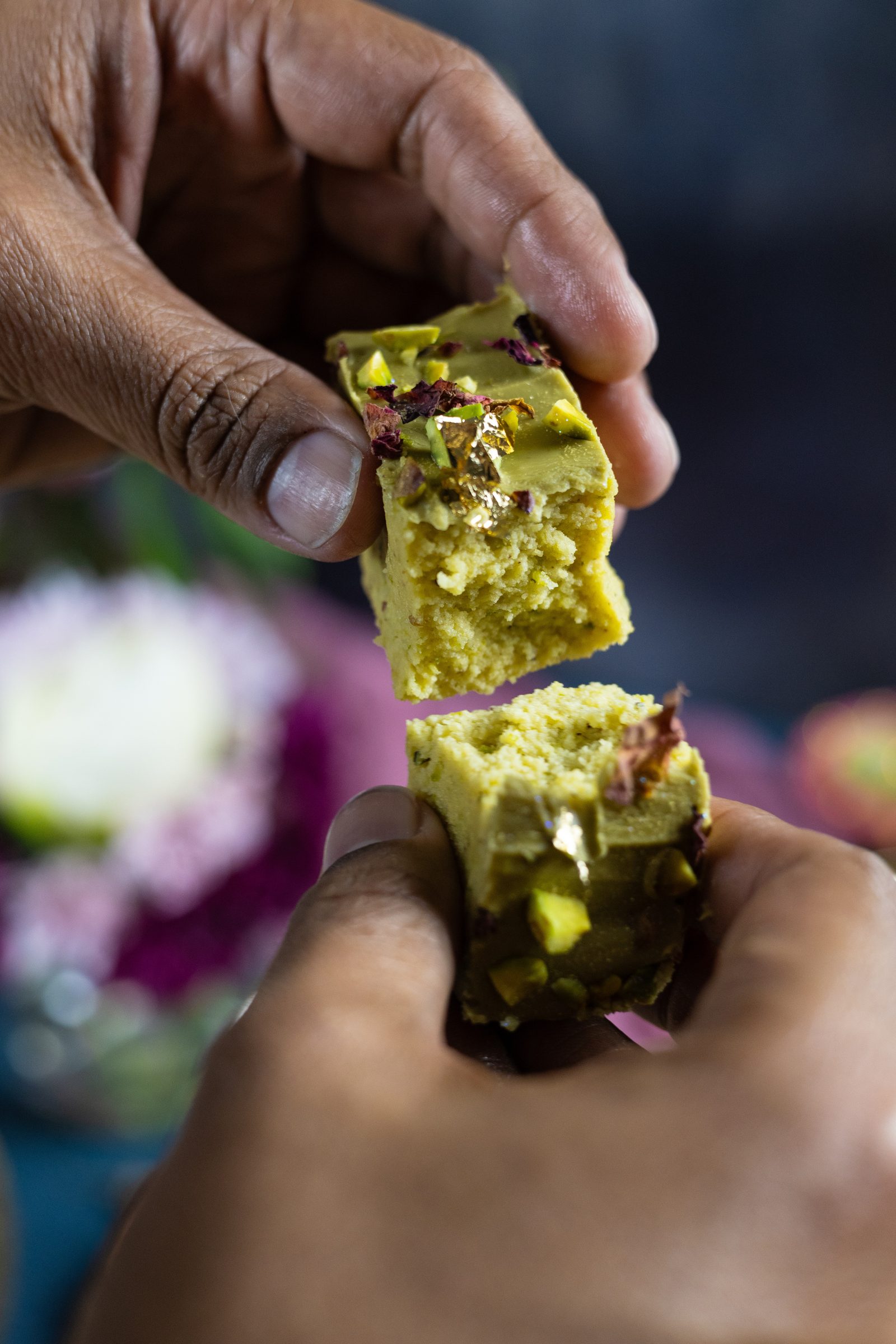 A piece of pistachio burfee broken in half, showing the soft inside under the pistachio topping