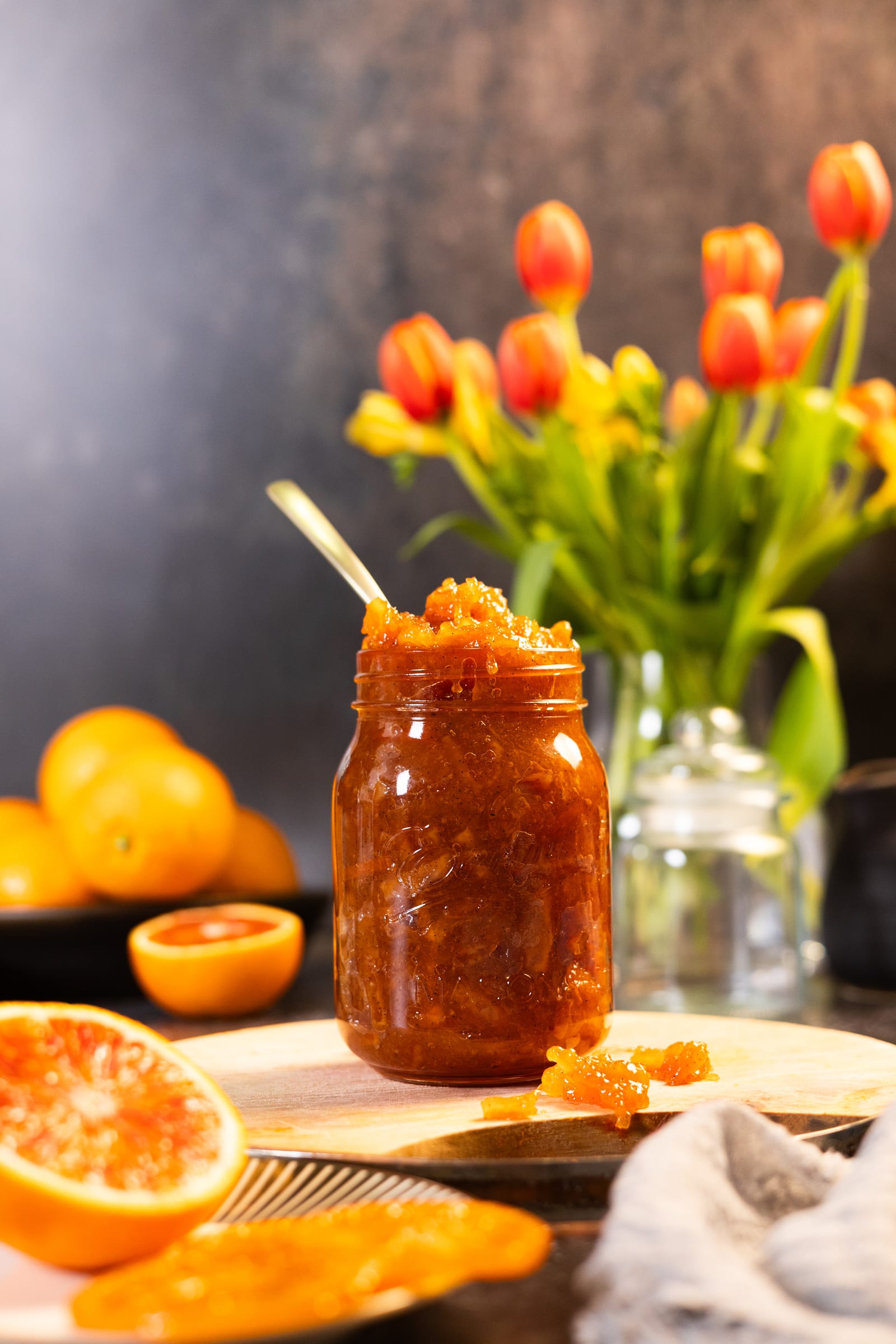 A jar of blood orange and brandy marmalade with red tulips and halved blood oranges
