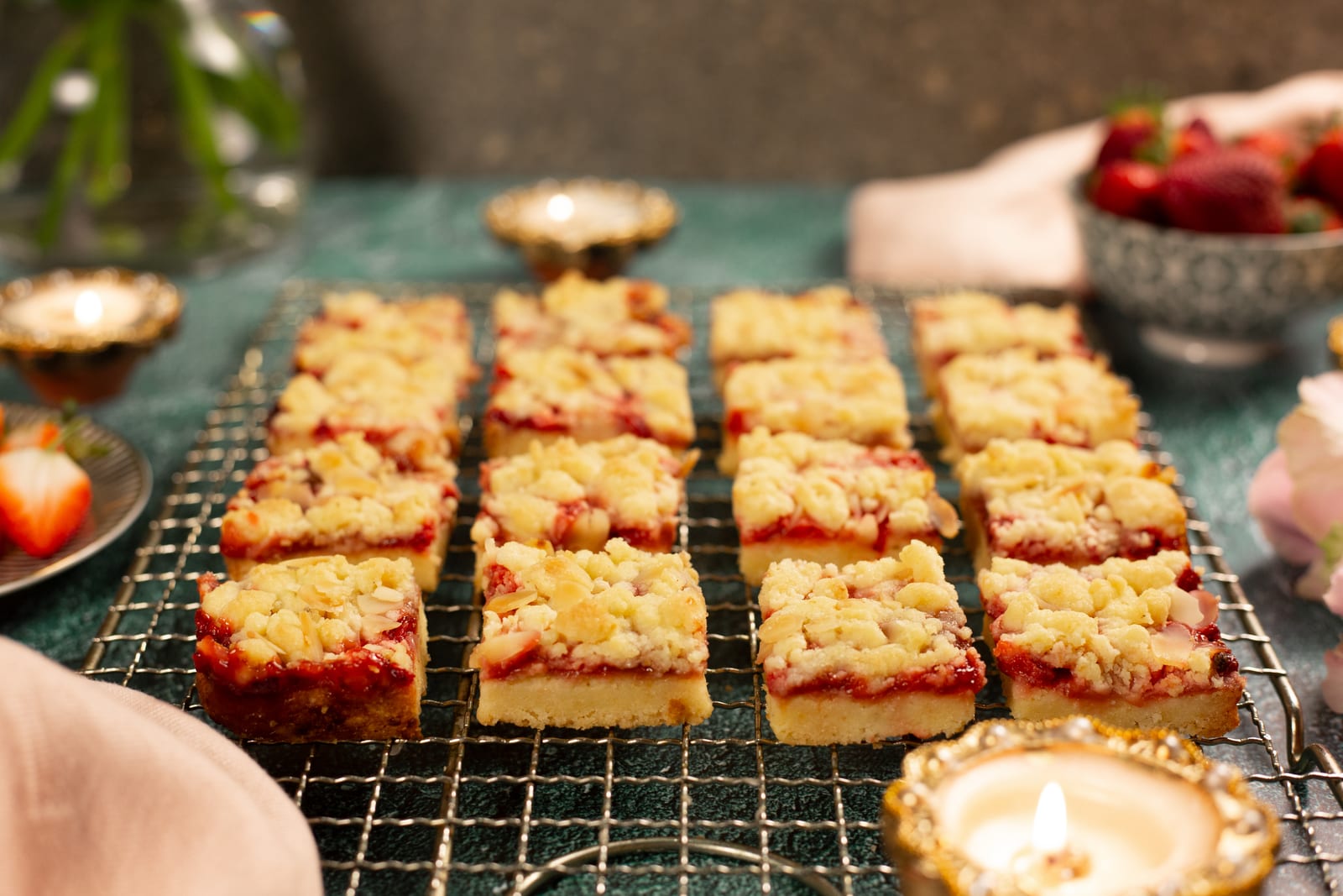 Squares of strawberry, lemon and almond Hungarian tart on a wire rack, with strawberries and a diya