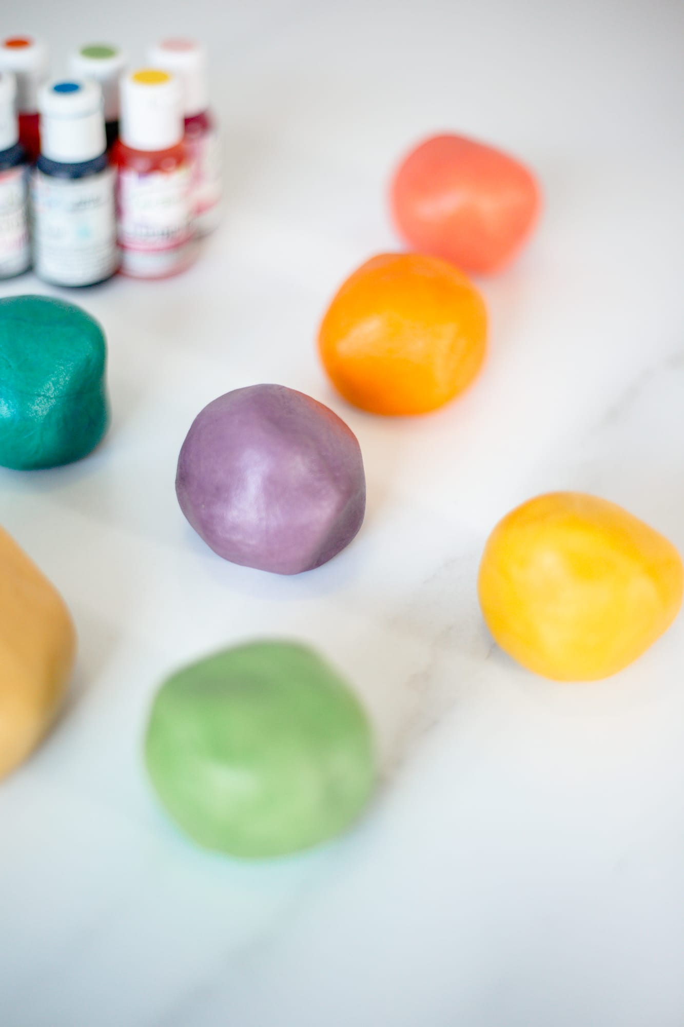 Balls of cookie dough tinted in six colours beside bottles of gel food colour