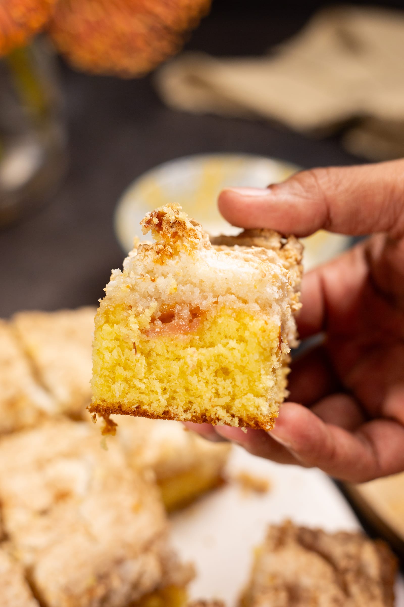 A hand holding up a hertzoggie square, showing the golden sponge under the coconut meringue