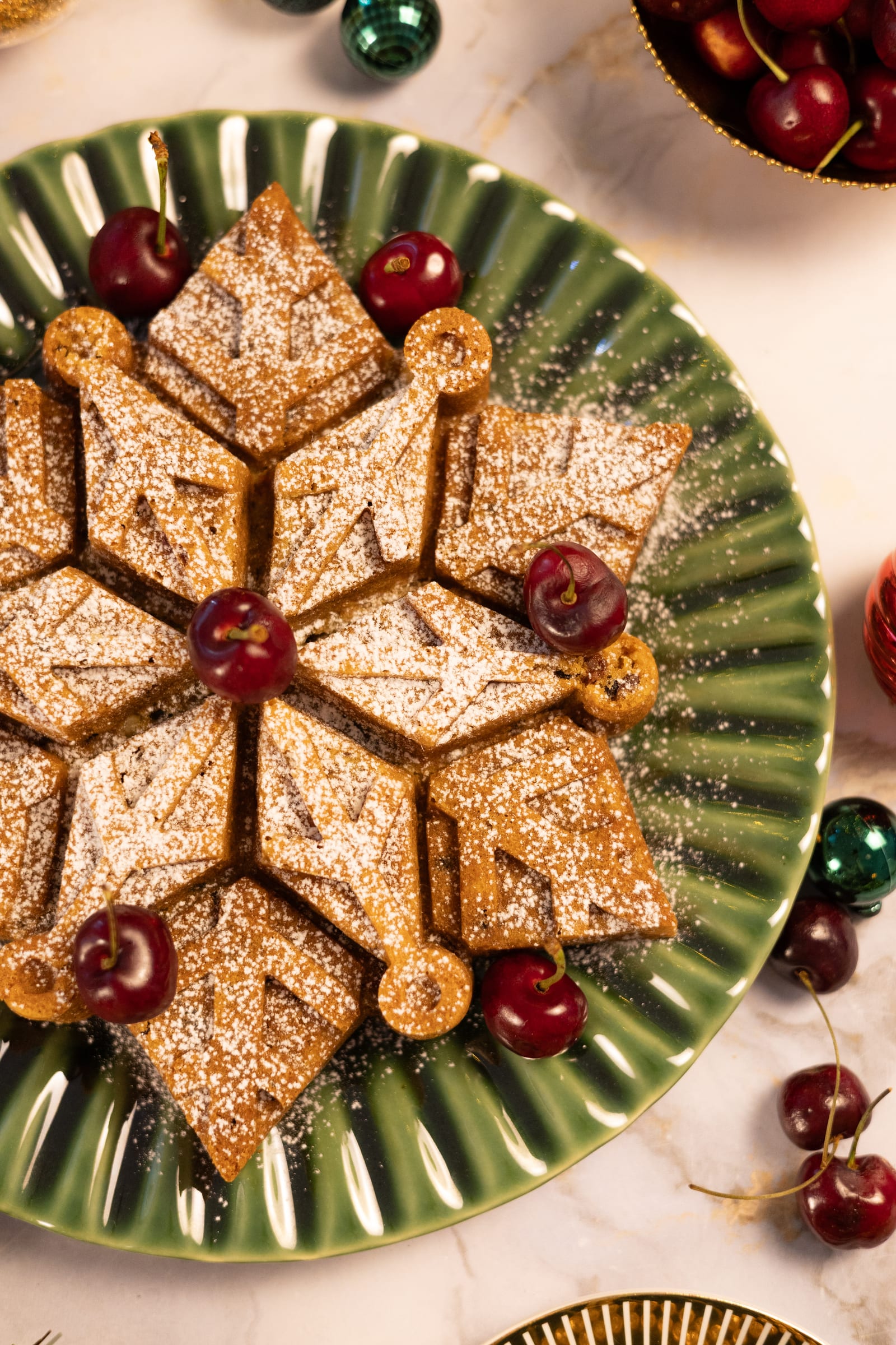 A snowflake-shaped fruitcake dusted with icing sugar, with cherries, from above