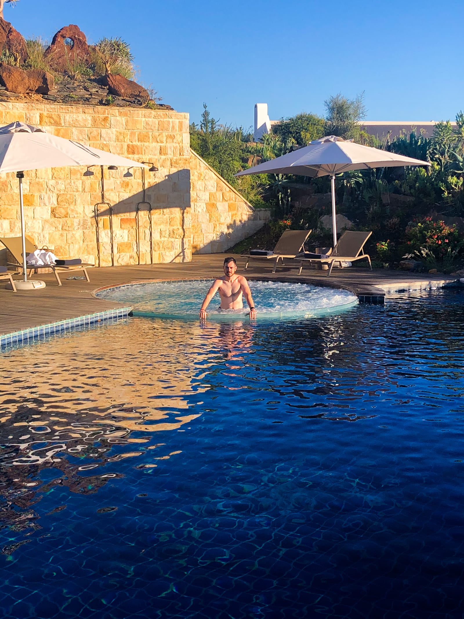 Linsen in the jacuzzi beside the heated pool at the Fynbos Cottages, with sun umbrellas, loungers and a sandstone wall