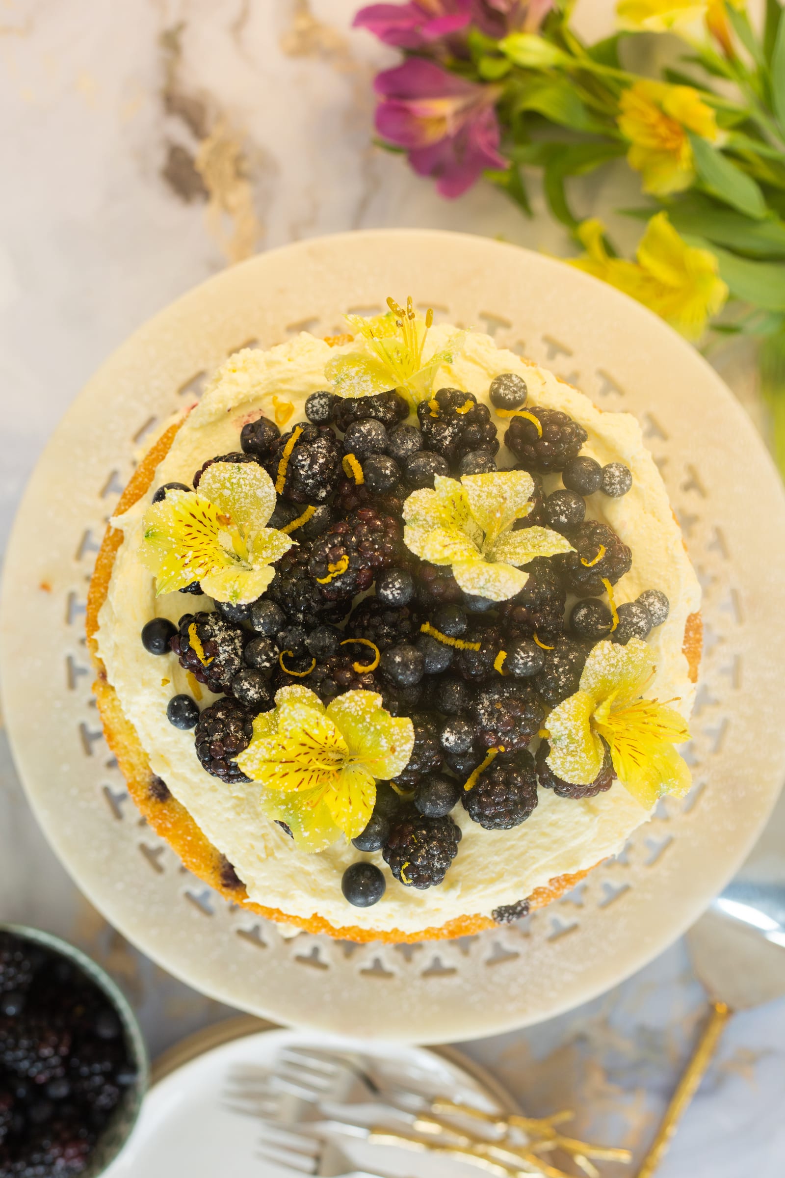 The top of the lemon and blueberry cake from above, heaped with berries and yellow flowers