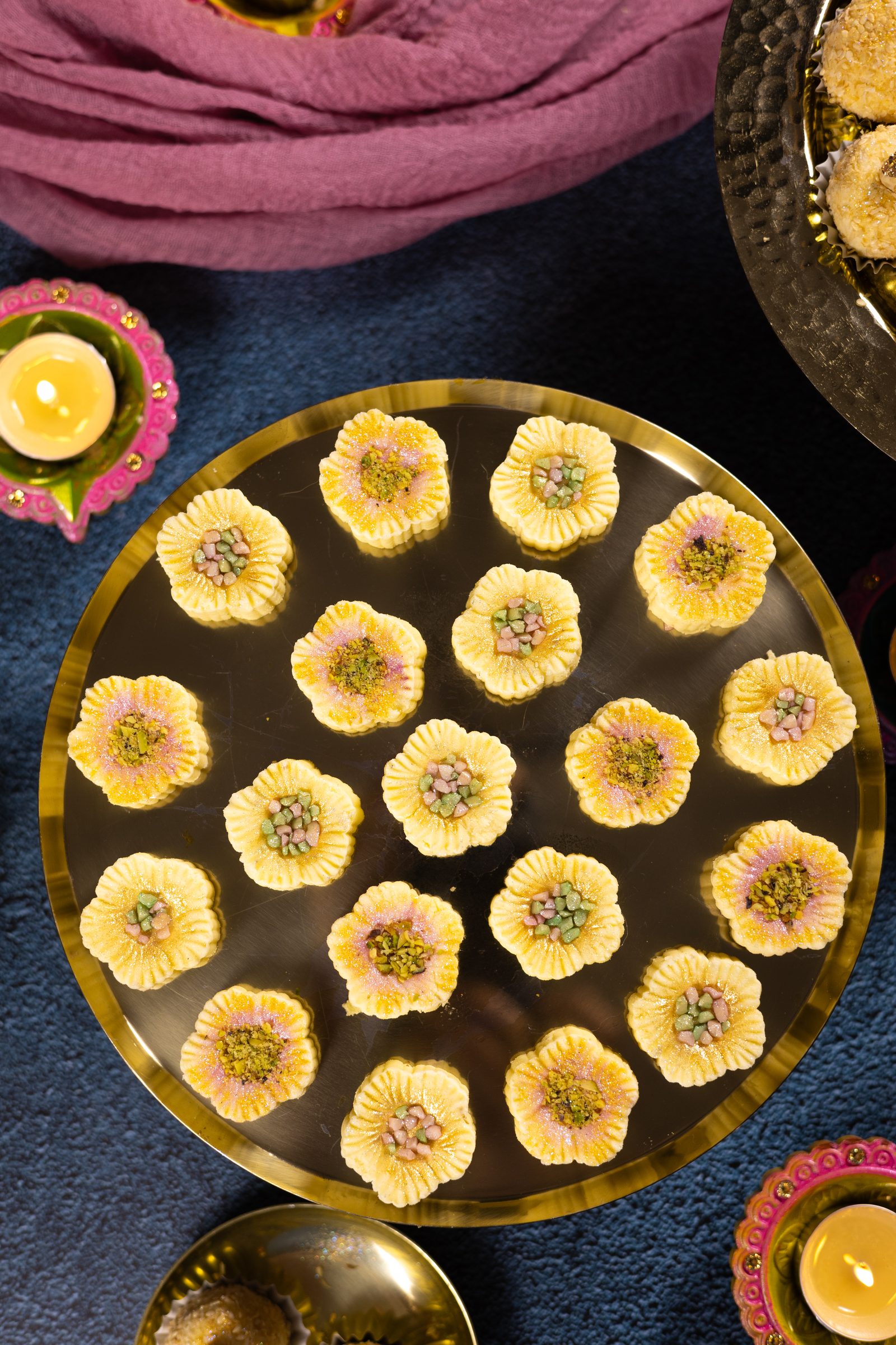 A gold plate of simply wonderfuls on a dark blue cloth with diyas, from above