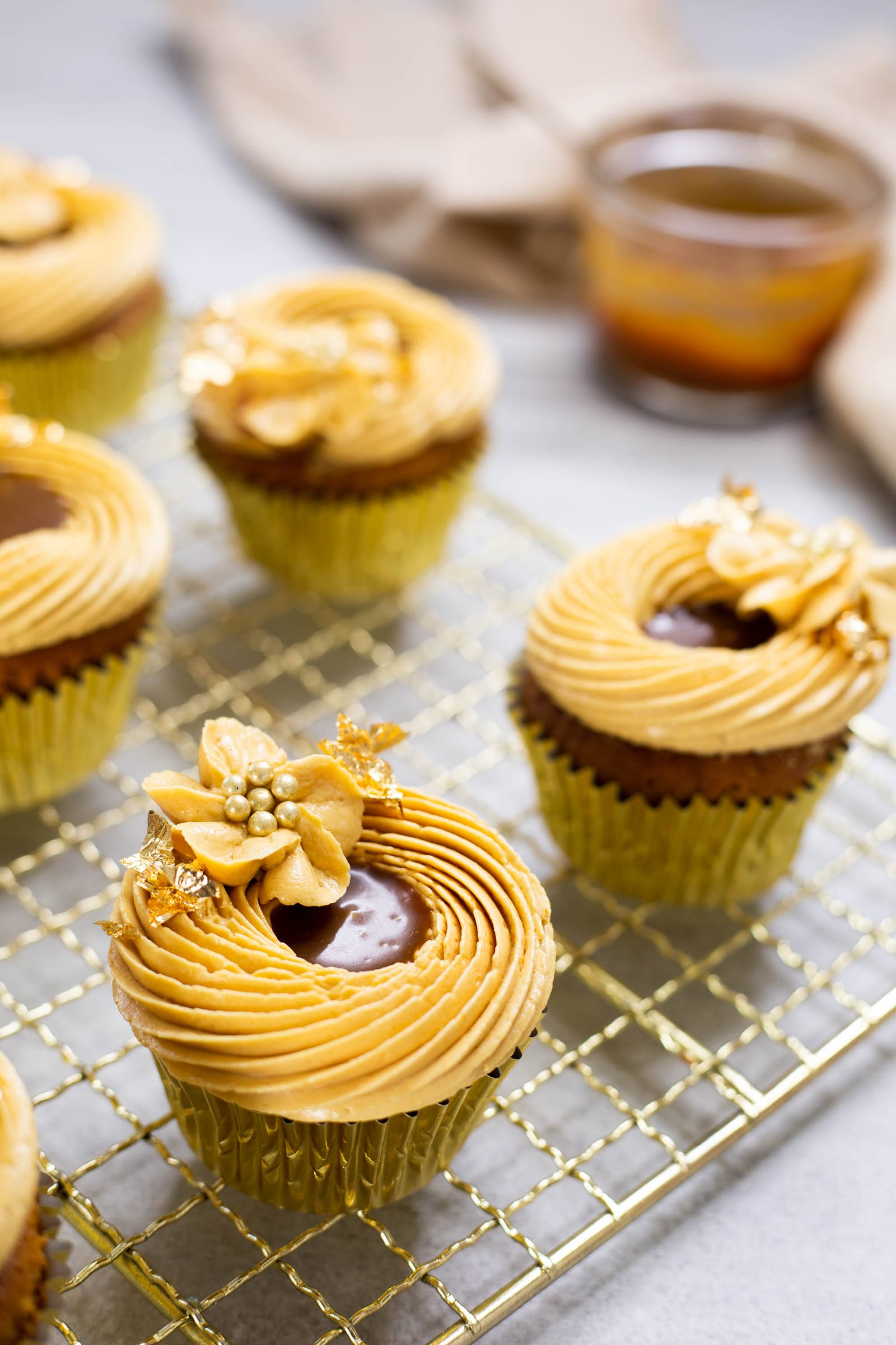 Close-up of a salted caramel cupcake with a swirl of caramel French buttercream, a caramel-filled centre and a gold sugar flower