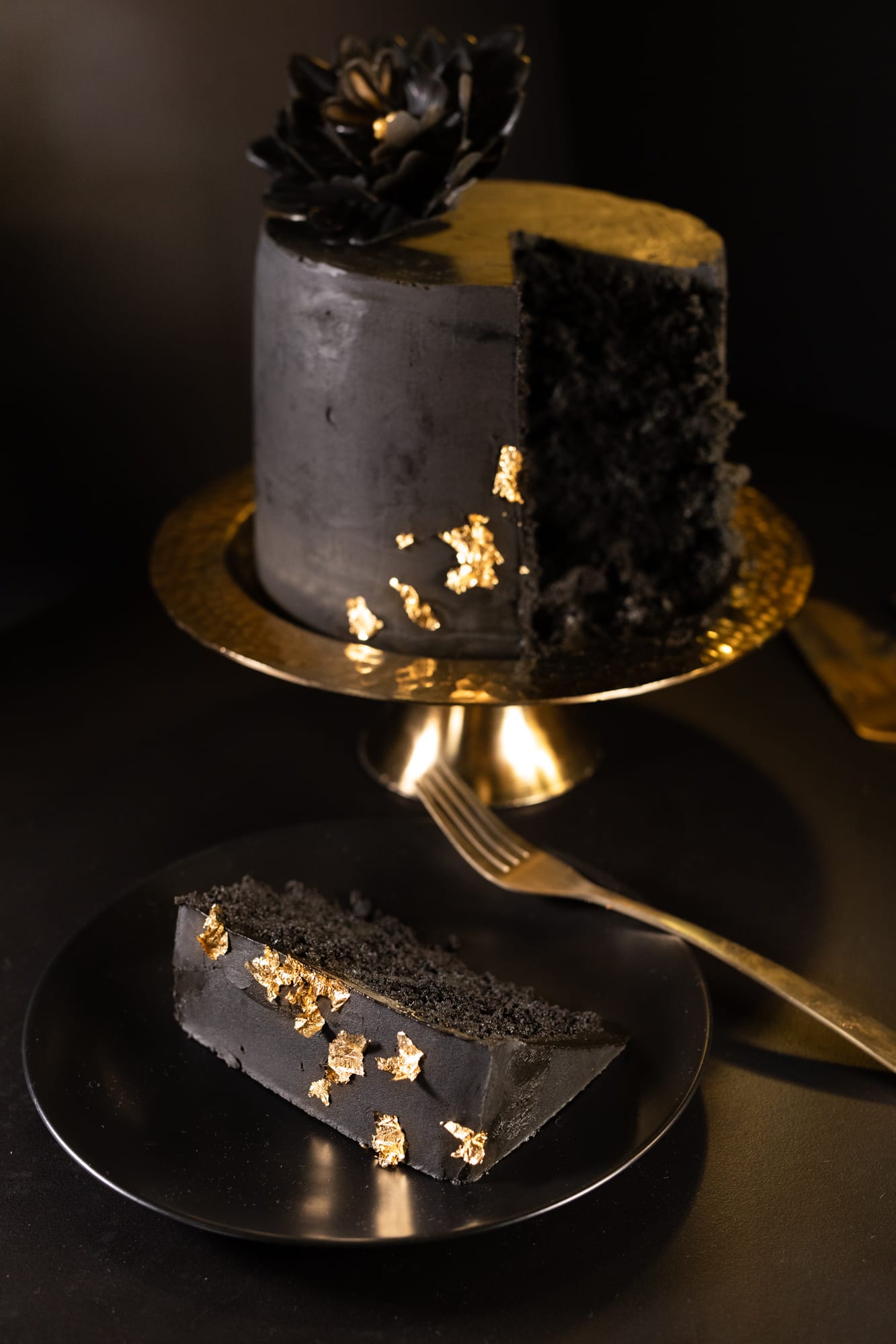A black velvet cake with a slice taken out, the slice on a black plate with a gold fork in front