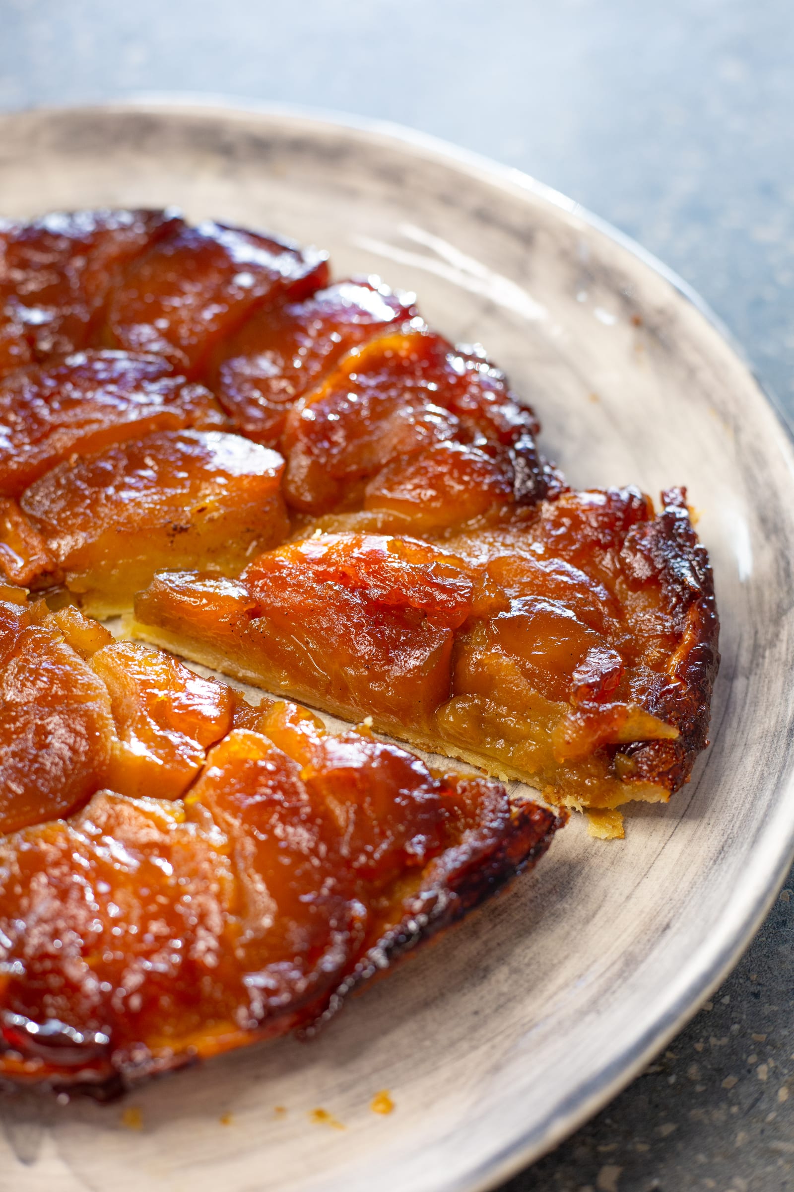 A wedge of apple tarte tatin pulled out, showing the puff pastry under the apples