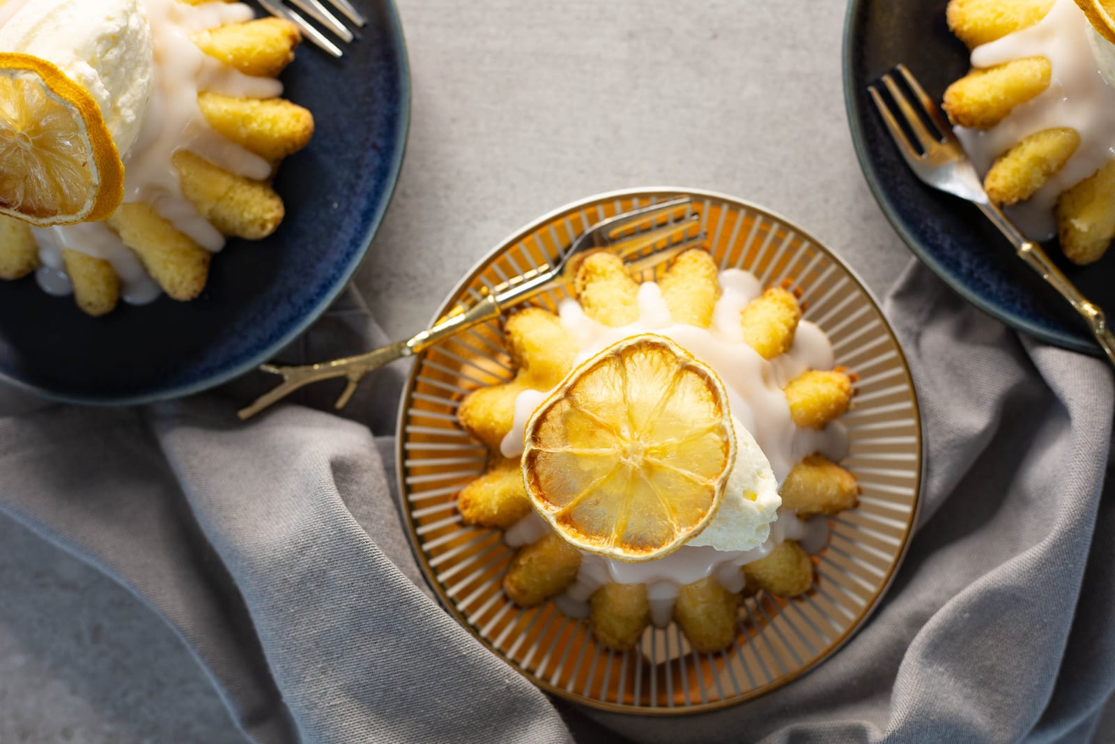 Semolina syrup cakes from above, glazed and topped with dried lemon slices, on gold and navy plates with forks
